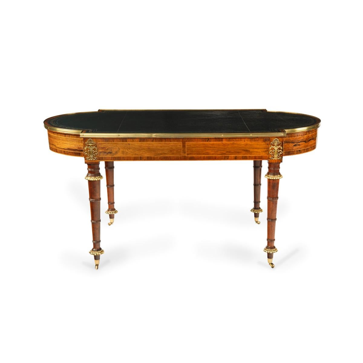 A Regency ormolu mounted rosewood two drawer writing table in the manner of John McLean and Gillows of Lancaster, the shaped rectangular top inset with tooled blue leather, with two cedar lined frieze drawers decorated with matching veneers and
