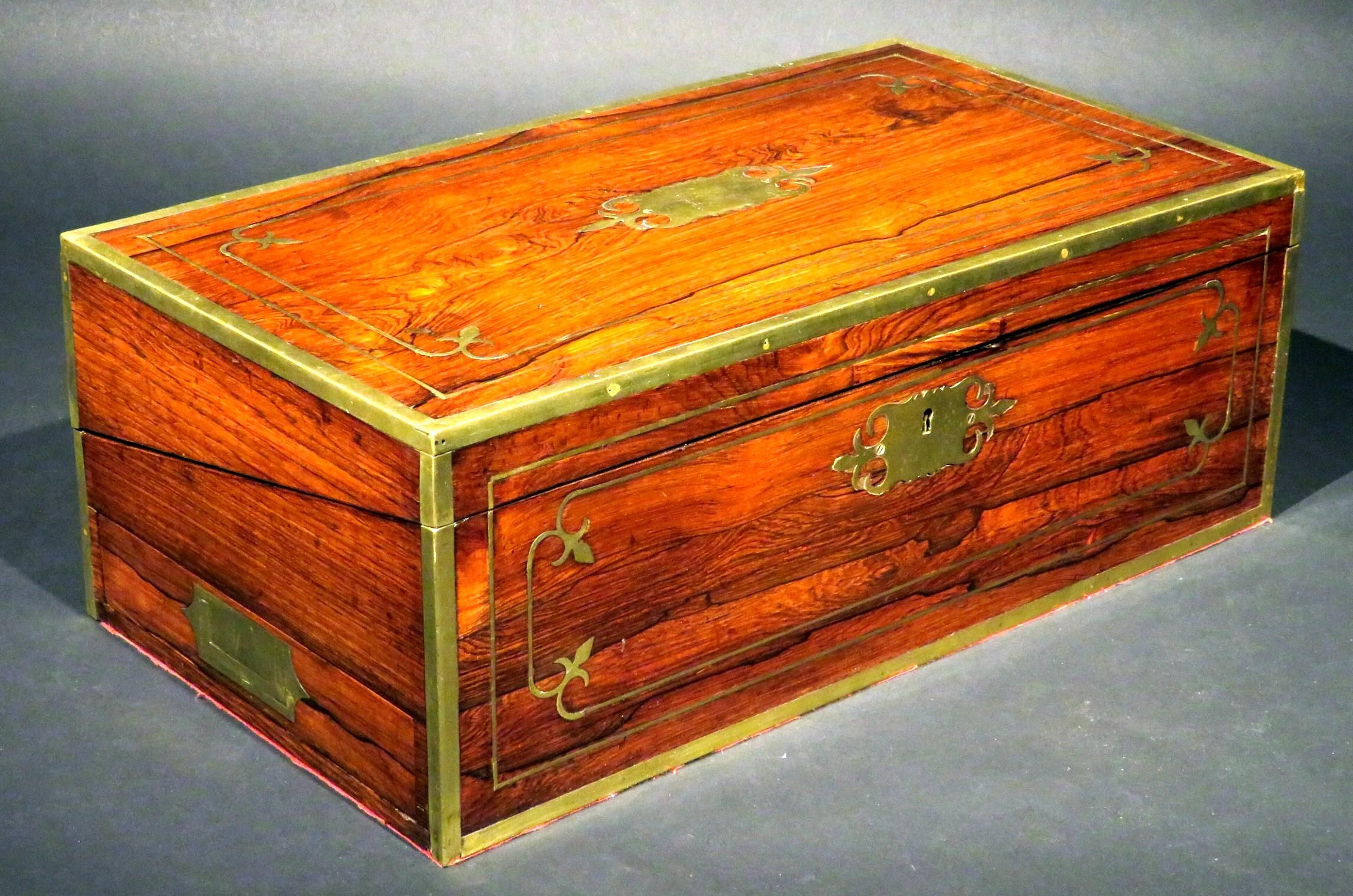 A superior Regency period brass bound writing box constructed of richly figured Brazilian rosewood, the hinged top inset with a blank brass cartouche and opening to an interior fitted for inkwells & writing implements, including two replace