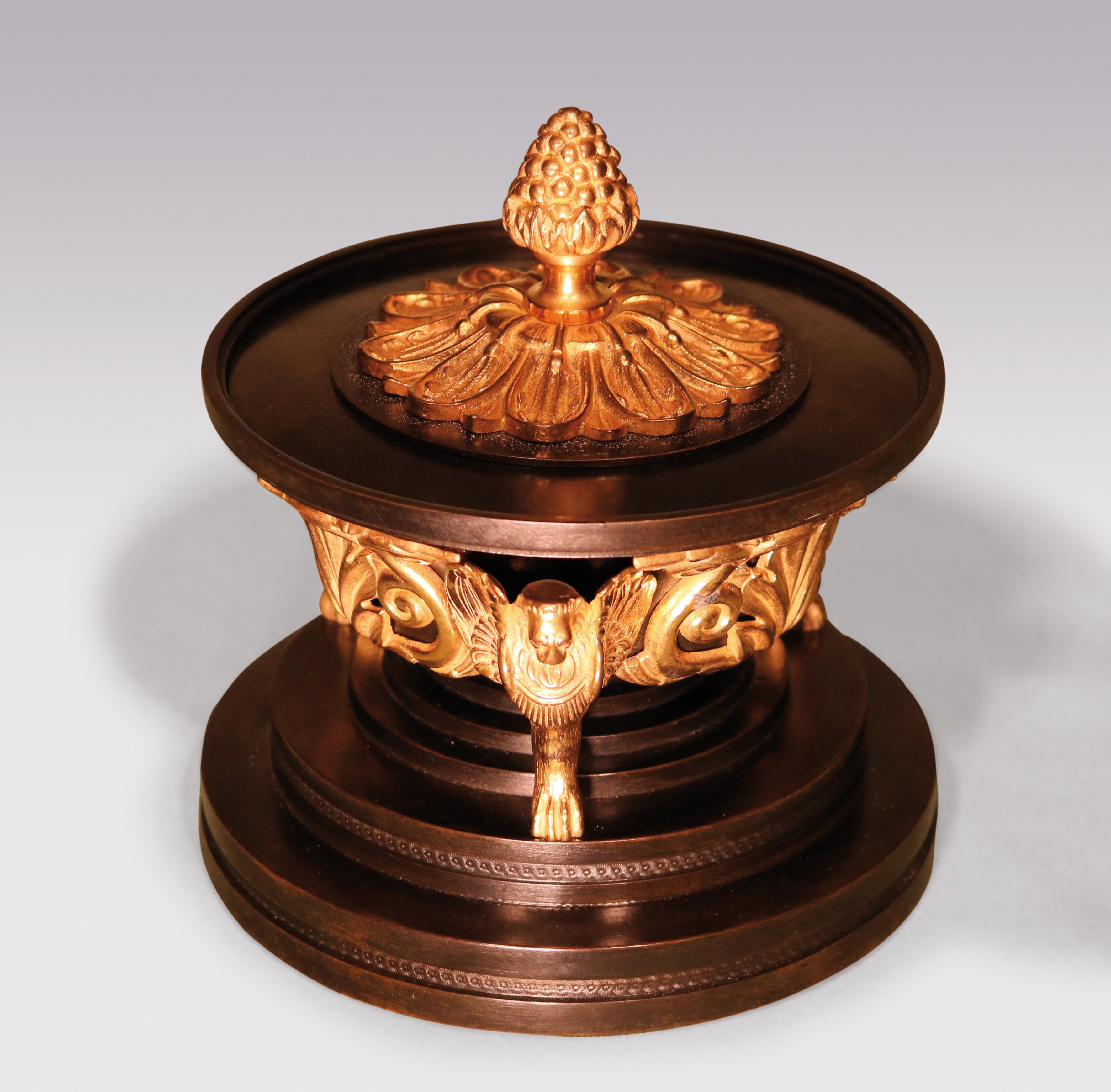 An unusual early 19th Century Regency period bronze & ormolu Tazza, having cover with pineapple finial, mounted with leaf & scroll decoration supported on winged lion monopodia ending on multi-stepped engine turned circular plinth base.