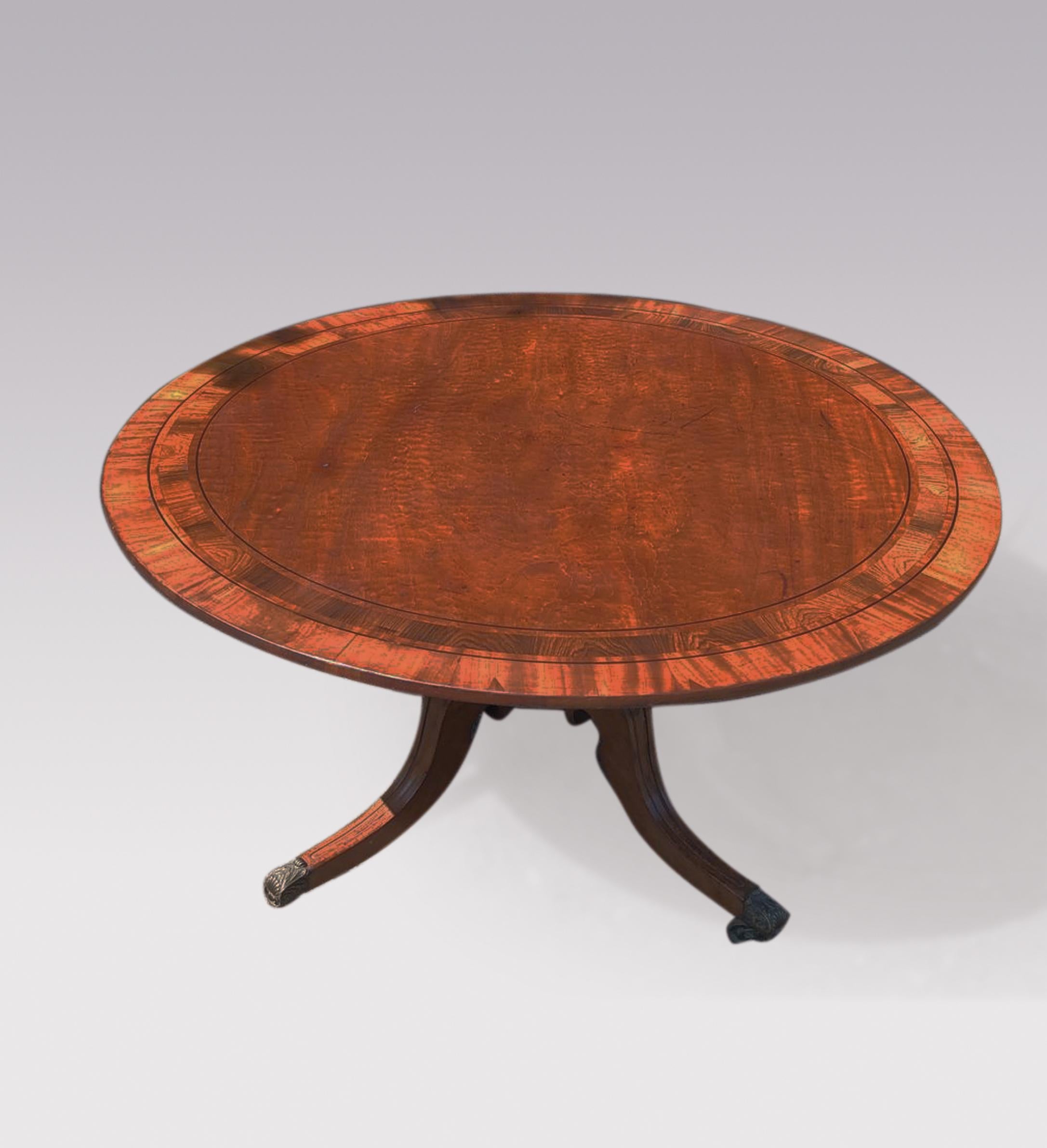 An early 19th century Regency period mahogany breakfast table having rosewood and mahogany double banded circular top supported on moulded panelled four splay base ending on original brass ‘shell’ castors.