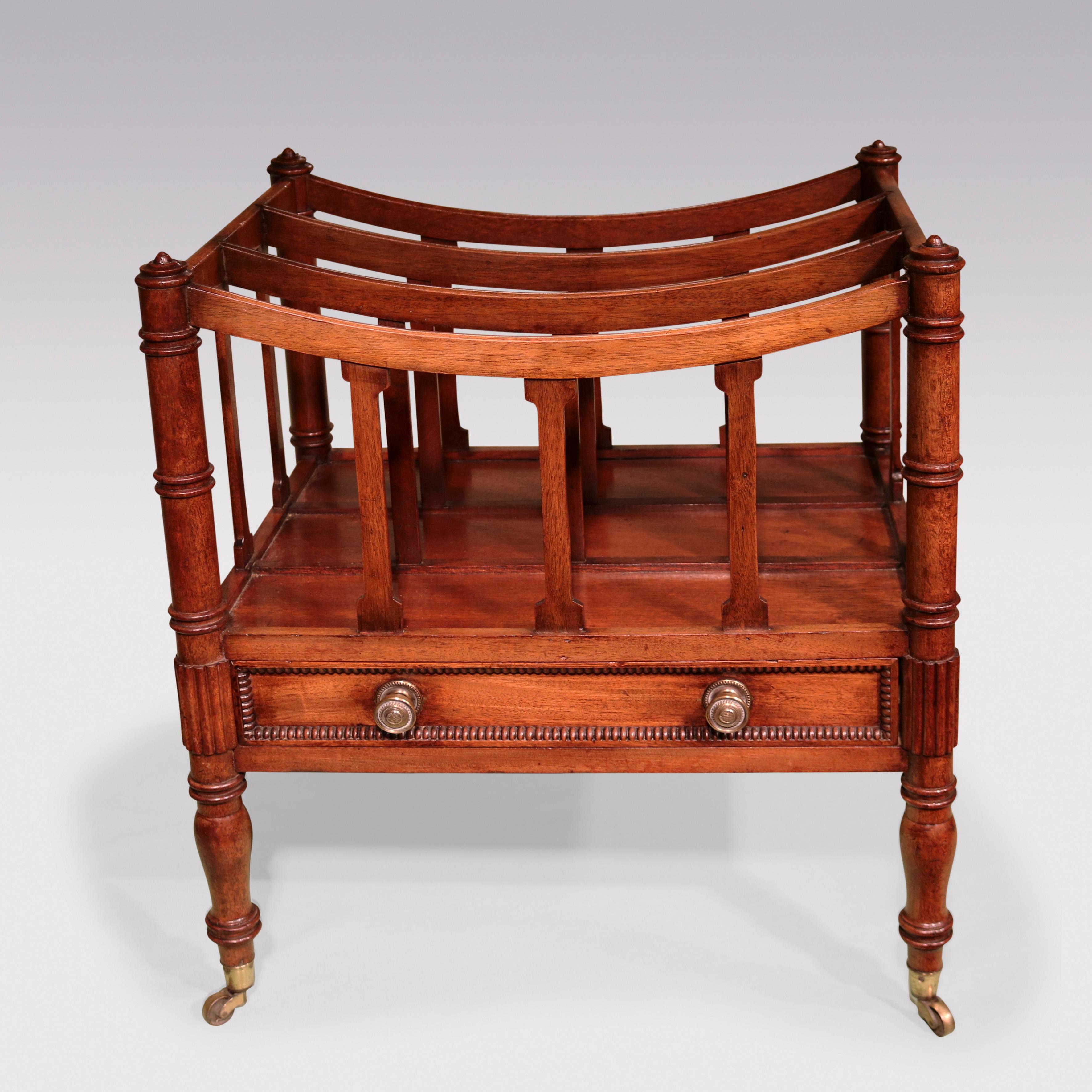 An early 19th Century mahogany concave shaped 4- section Canterbury, having ring-turned corner columns above beaded frieze drawer flanked by unusual reeded carving supported on baluster turned legs ending on original brass castors.