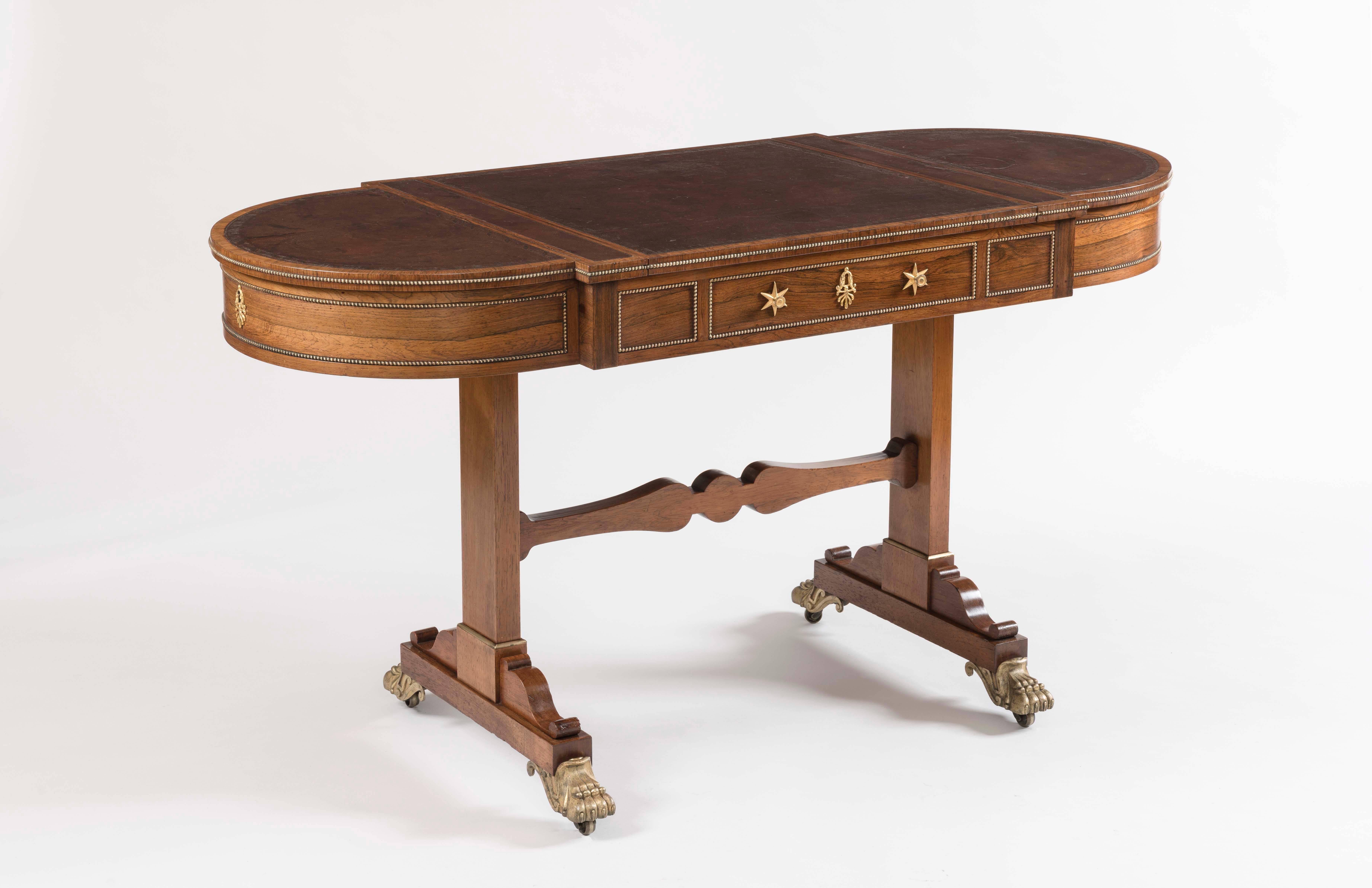 A Regency period games table
firmly attributed to Gillows of Lancaster.
 
Constructed in Gonçalo Alves; of end support form, braced with a central shaped stretcher; the spandrel form leaf carved truss bases terminate with crisply carved cast