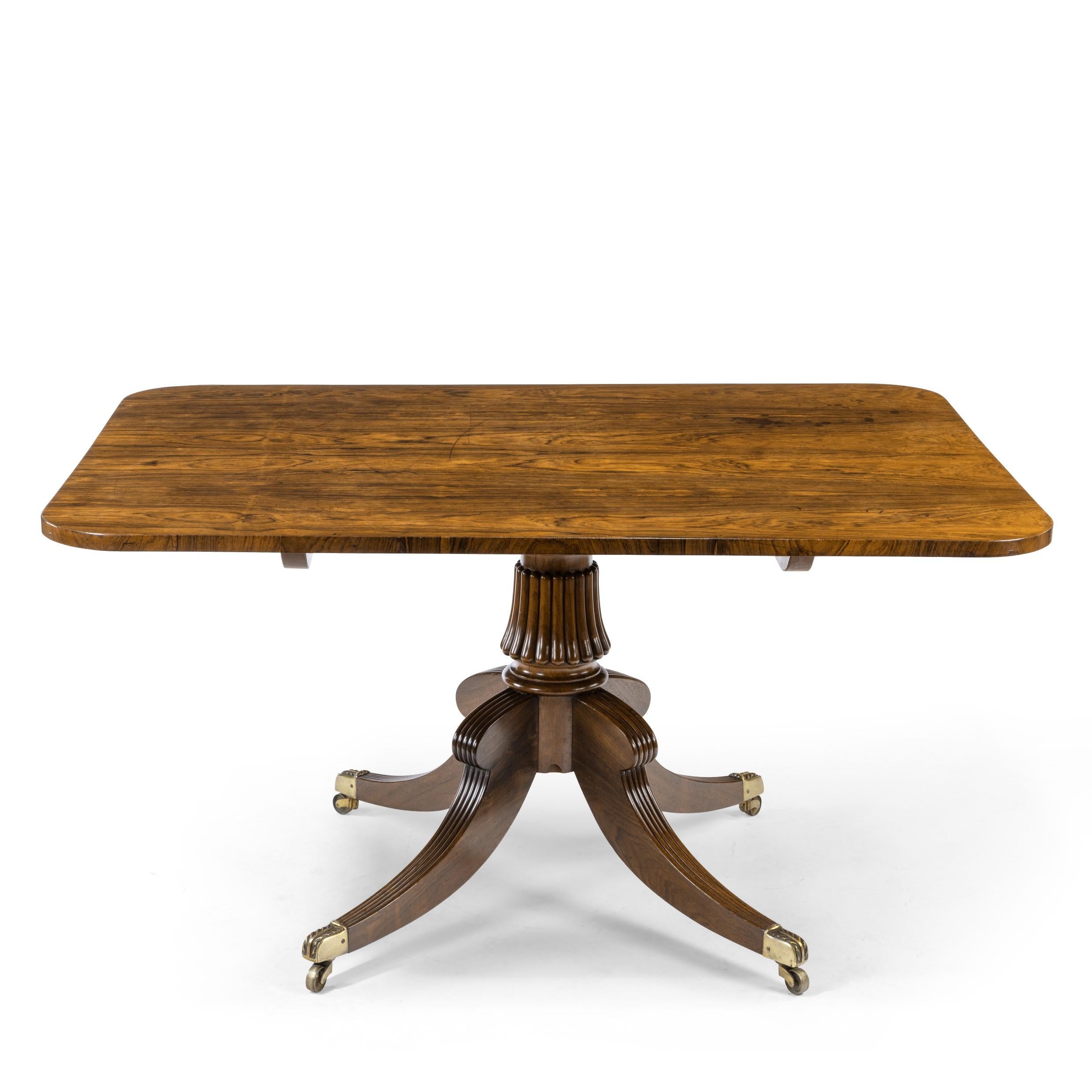 A Regency rectangular rosewood tilt-top table attributed to Gillows, the rectangular top with bookmatched veneers set upon a shaped and reeded support with four splayed hip legs, English, circa 1815.
  