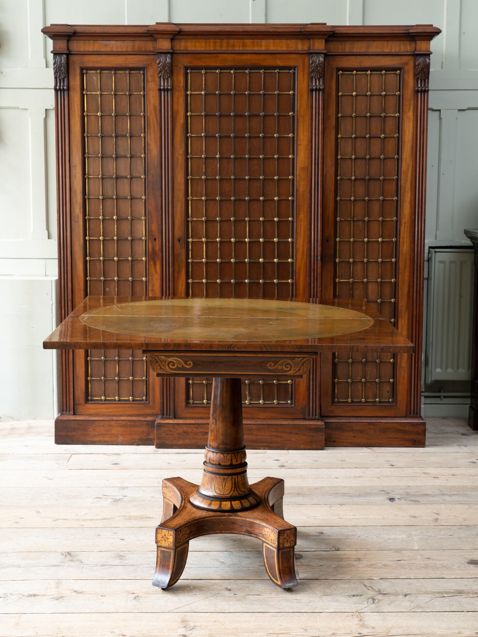 The rectangular fold over top raised on a tapering cylinder pillar with overall painted faux wood grain and pen work decoration on a quatrefoil base, inset caster to the shaped feet.

A highly original example, only the tooled leather top is not