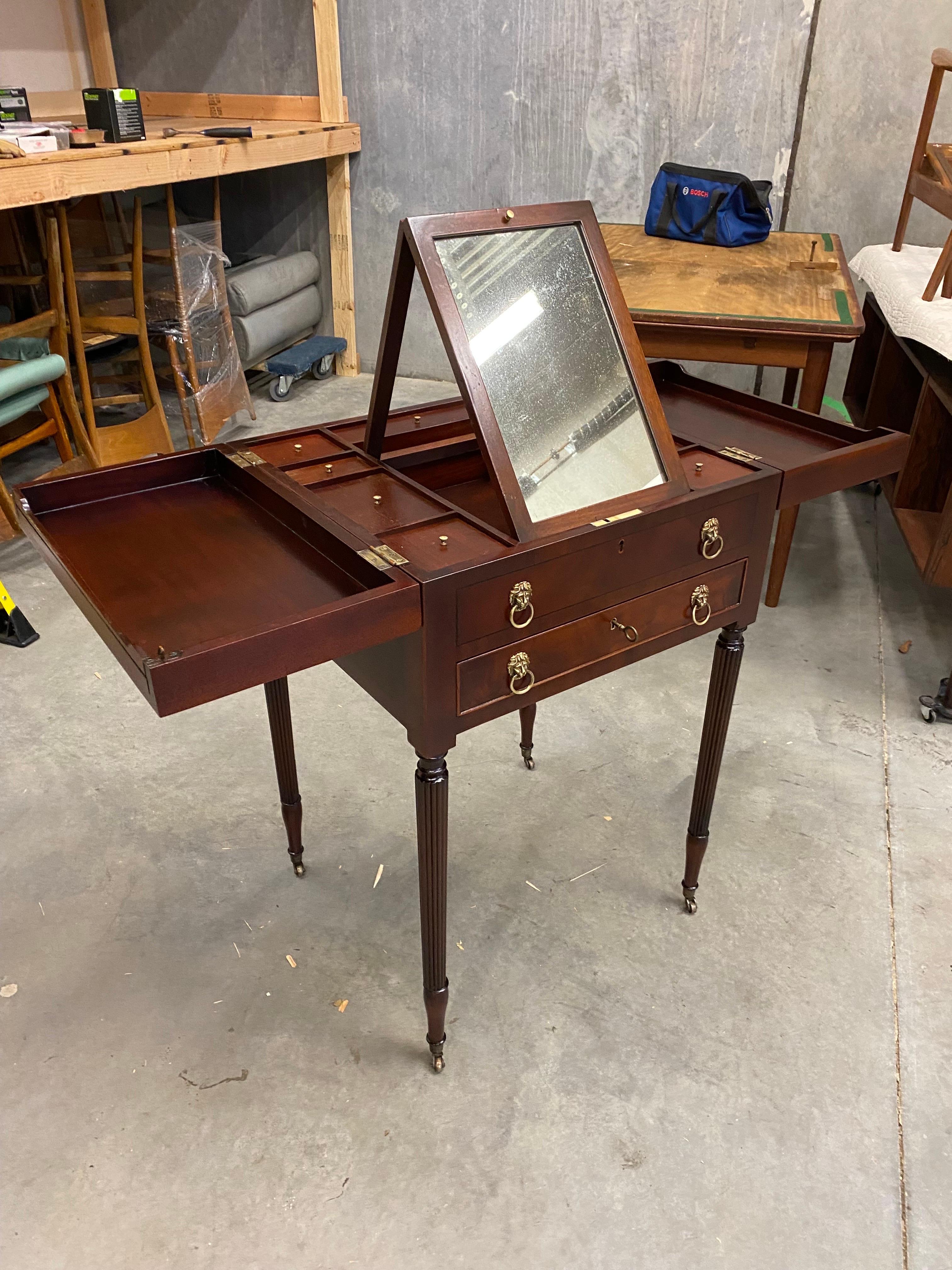 A Regency style carved mahogany Beau Brummel gentleman's dressing table, 20th century, the hinged top enclosing nine lidded compartments about a folding mirror, with one faux and one genuine drawer to the frieze below, the genuine drawer fitted with