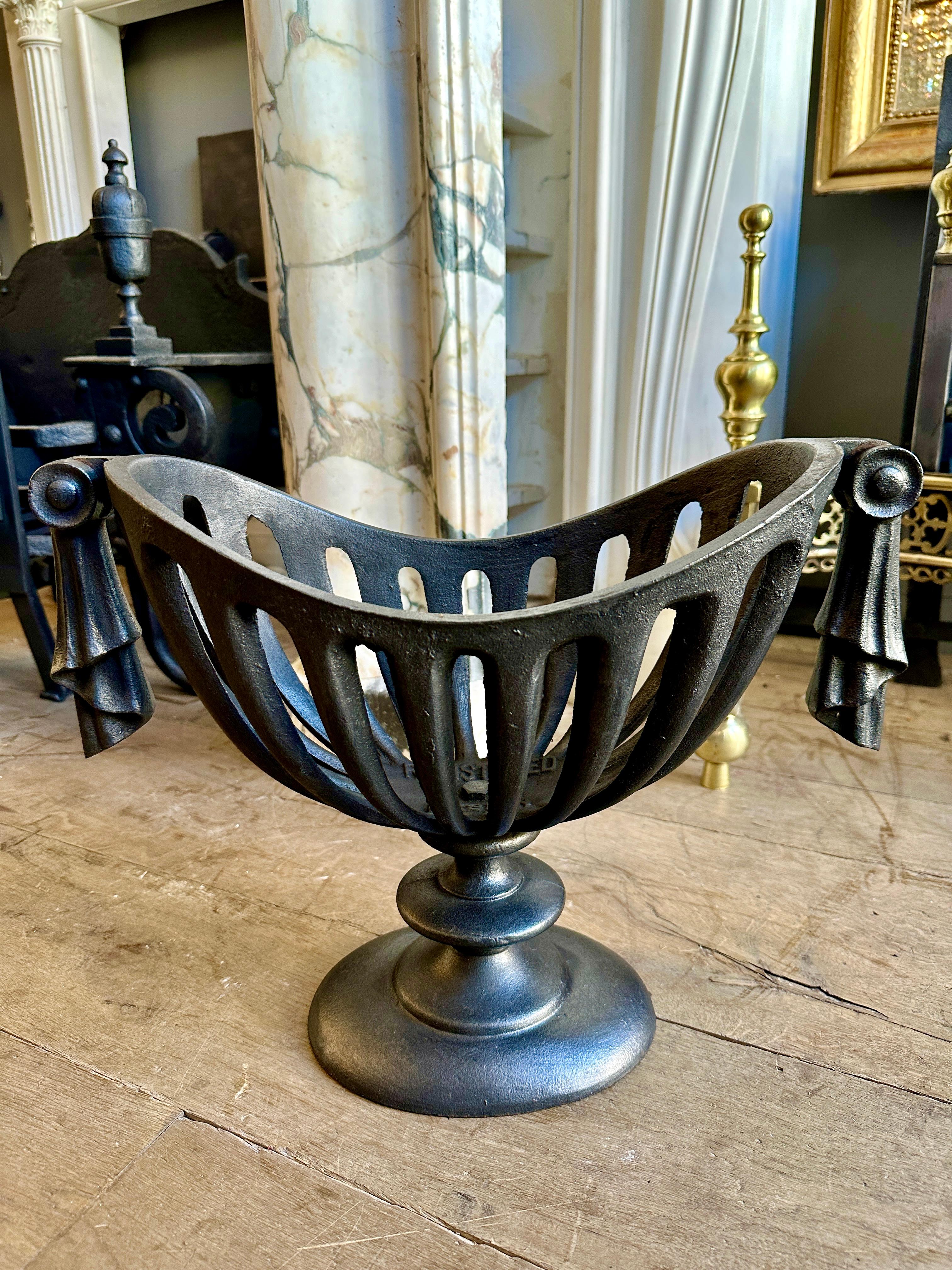 A small regency style cast iron urn grate. Stood on an architectural style soccle with open fluted burning area. Swag draping from either end. Black lead polished finish. Perfect grate for smaller openings.