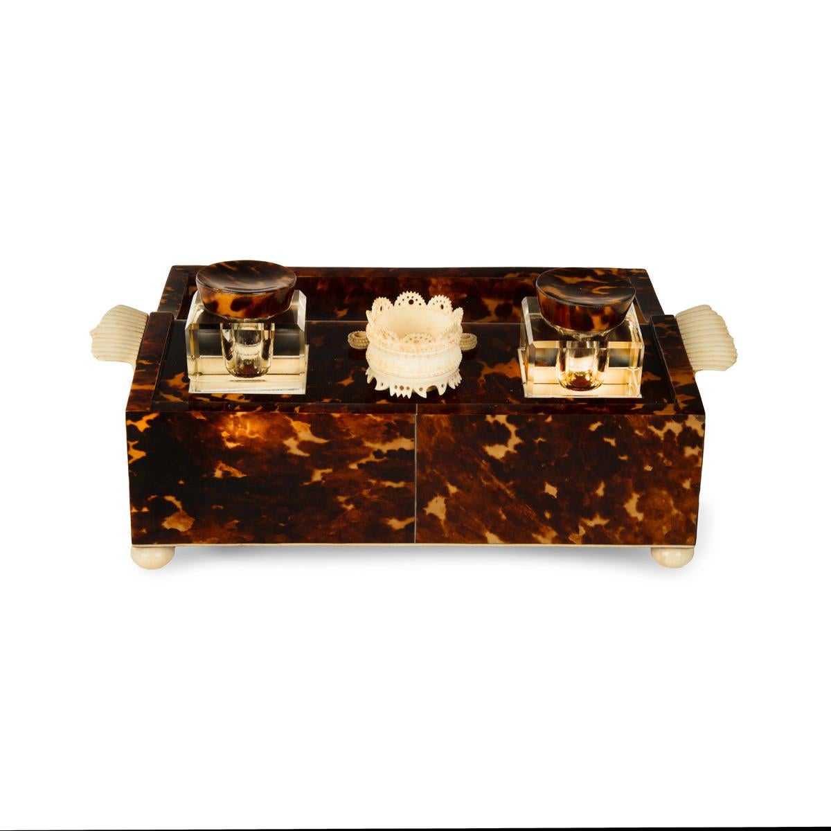 A Regency tortoiseshell and ivory desk set, of shaped rectangular form with two glass inkwells, an ivory pot and two ivory pen holders above a curved pen tray with a single frieze drawers, with gadrooned carrying handles, a turned knop handled and