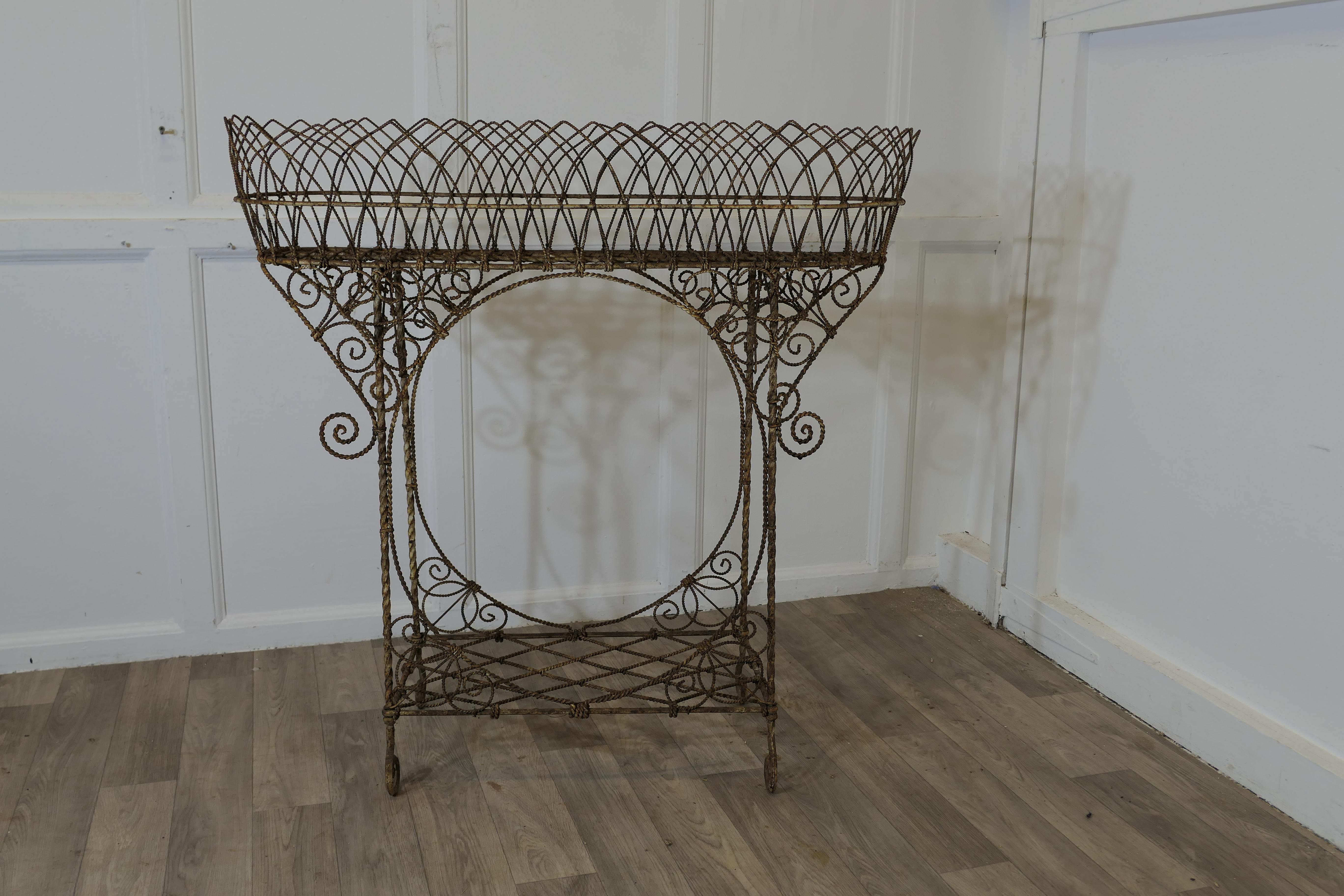 Un portavaso Regency in filo metallico

La fioriera ha un cesto superiore e un ripiano inferiore, e poggia su piedi arricciati.
Si tratta di un eccellente pezzo di ferro battuto a mano, in ottime condizioni per la sua età, tutto il filo è