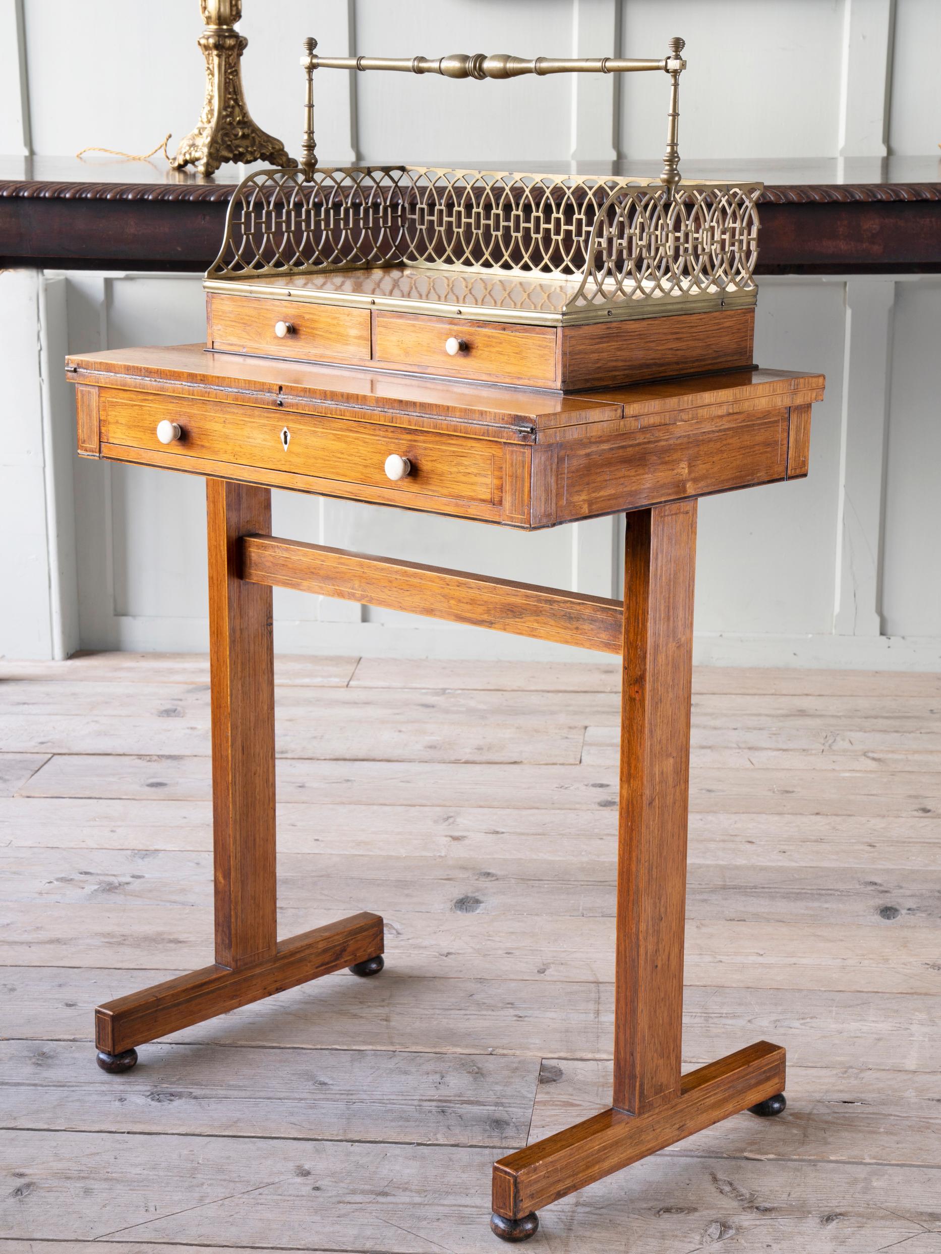 The rosewood table on trestle base has a folding writing surface with leather insert above a single drawer, the book carrier (Cheveret) with twin drawers and a pierced brass gallery, the whole with fruitwood banding and brass beading.

The desk