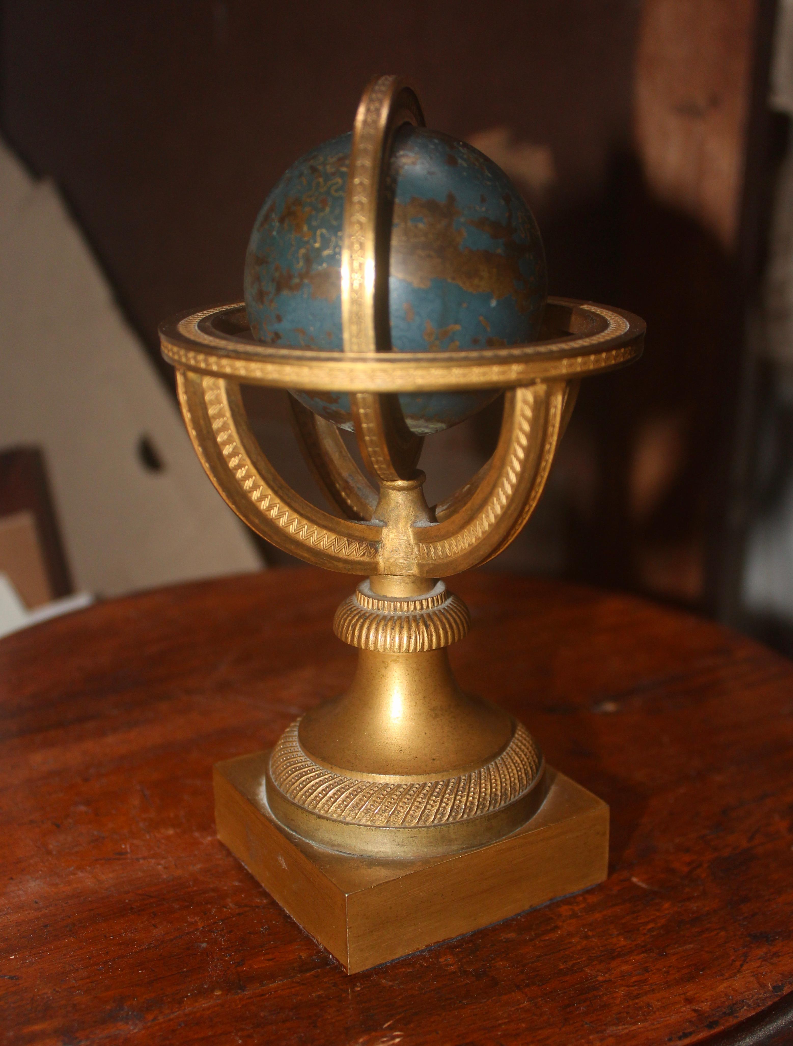 A Restauration gilded bronze and blue epargne armillary sphere and paperweight
finely chiseled and gilded bronze, the sphere in blue and gold enameled copper, resting on a pedestal and a square base,
circa 1830.
