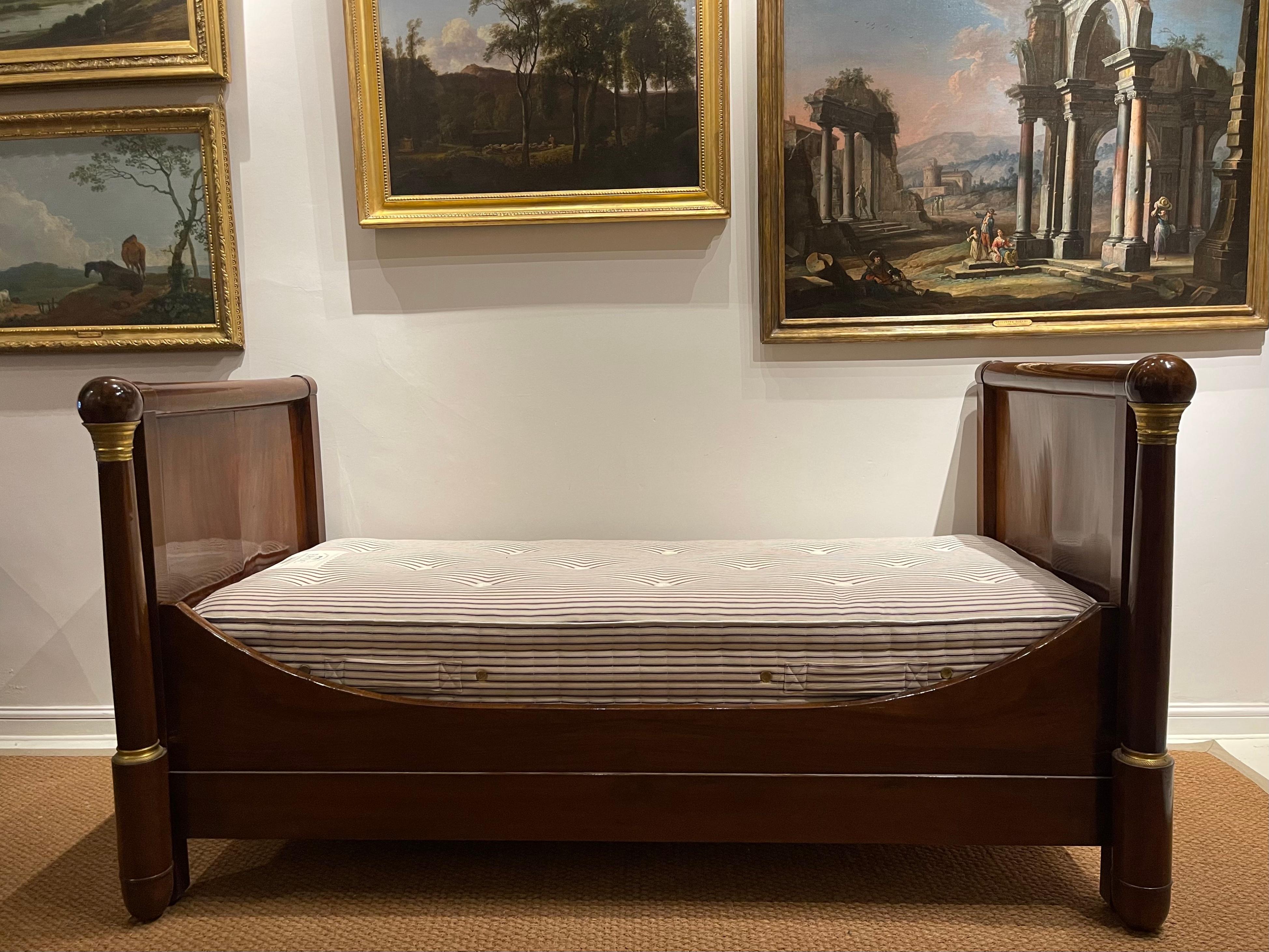 A Restauration Napoleonic Empire Ormolu-Mounted mahogany day bed (Early 19th Century).

The structure consists of solid mahogany. The outward facing ends are each joined to a column, each surmounted by a solid mahogany ball. Ormolu embellishes