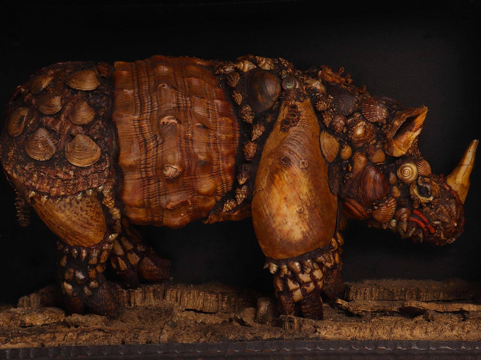 A Wunderkammer natural specimen: the Rhinoceros. A sculpture depicting a rhinoceros, made out of different shells, coral, mother of pearls. The rhinoceros stand on a cork wood. Mounted on black wooden support. The frame is made out of a black
