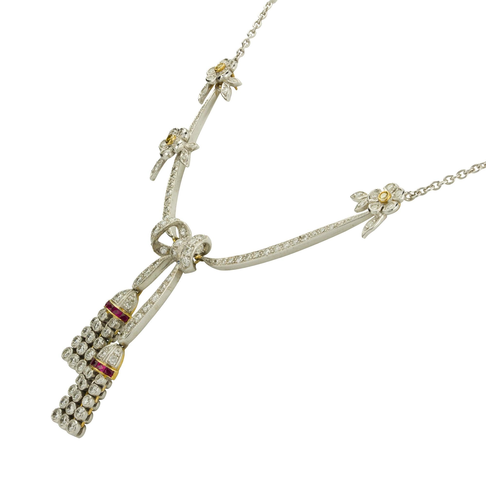 A ribbon-like diamond and ruby necklace, to the centre a diamond-set bow terminating to two diamond tassels with calibre-cut ruby-set caps, the bow suspended by two ribbon-like diamond-set links, the one set with two and the other with one