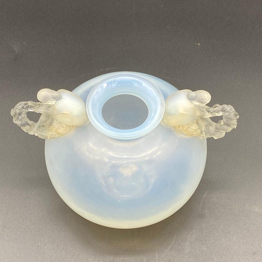 Il vaso Bouchardon è stato creato nel 1926 da R.Lalique in vetro bianco.

Questo esemplare è in vetro opalescente profondo con corpo lucido e maniglie applicate smerigliate.

I manici sono applicati a mano sul corpo del vaso.

Il vaso ha un blocco