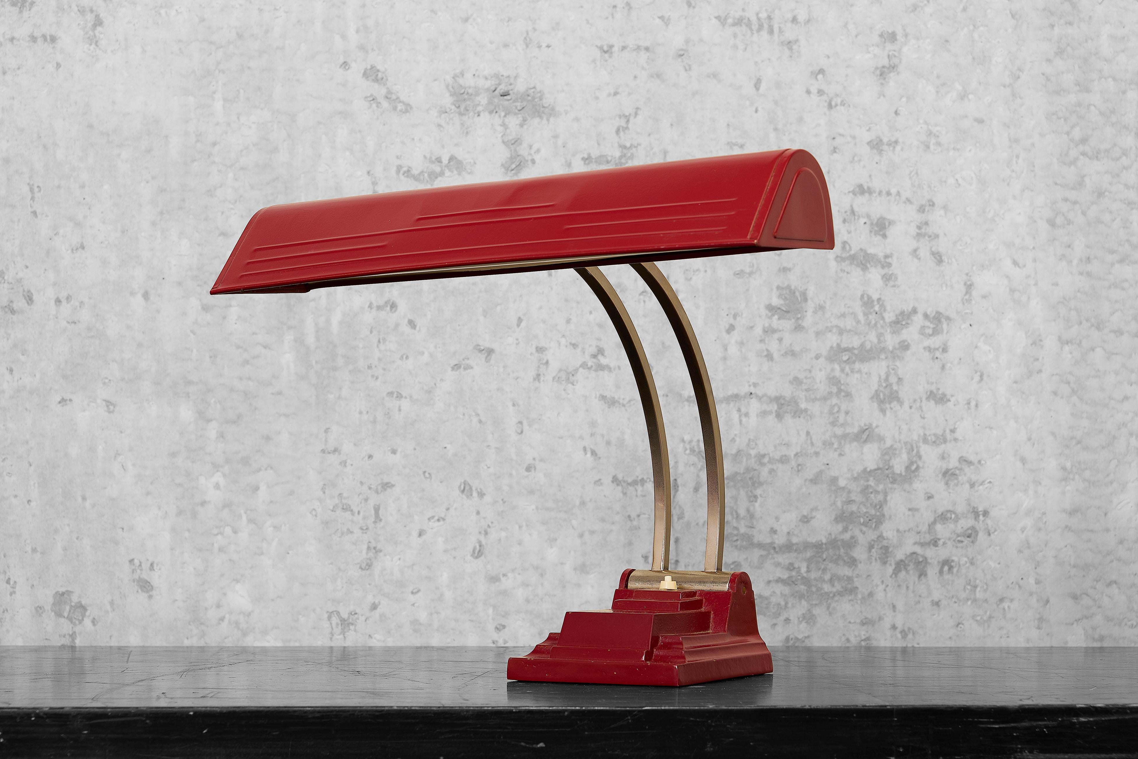 Lampe de bureau industrielle robuste de couleur rouge bordeaux avec une lumière fluorescente. La lampe a une base solide et lourde en fer rectangulaire, une tige incurvée en chrome et un abat-jour à charnière. La lampe a été repeinte et recâblée. La