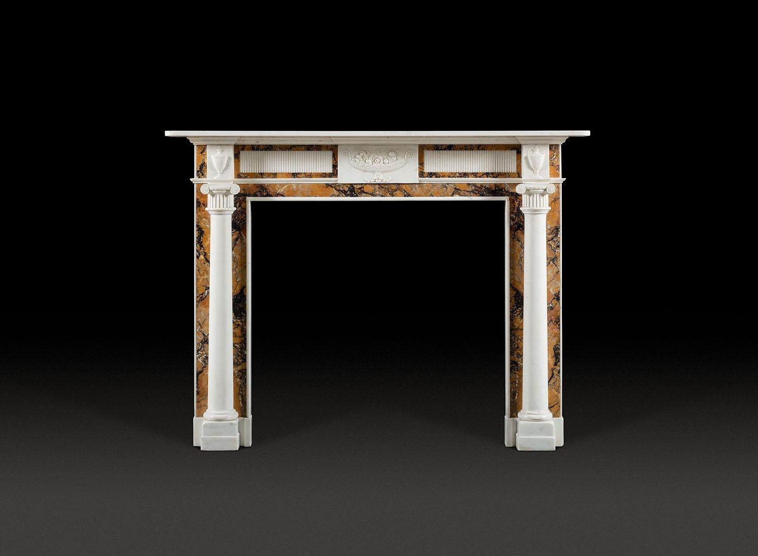 A Robust, Regency period and Style Chimneypiece in Statuary and Convent Sienna Marbles.

With plain rectangular shelf raised on bed mouldings above the sienna frieze. The frieze centred with a neo classical statuary tablet decorated with a tazza,