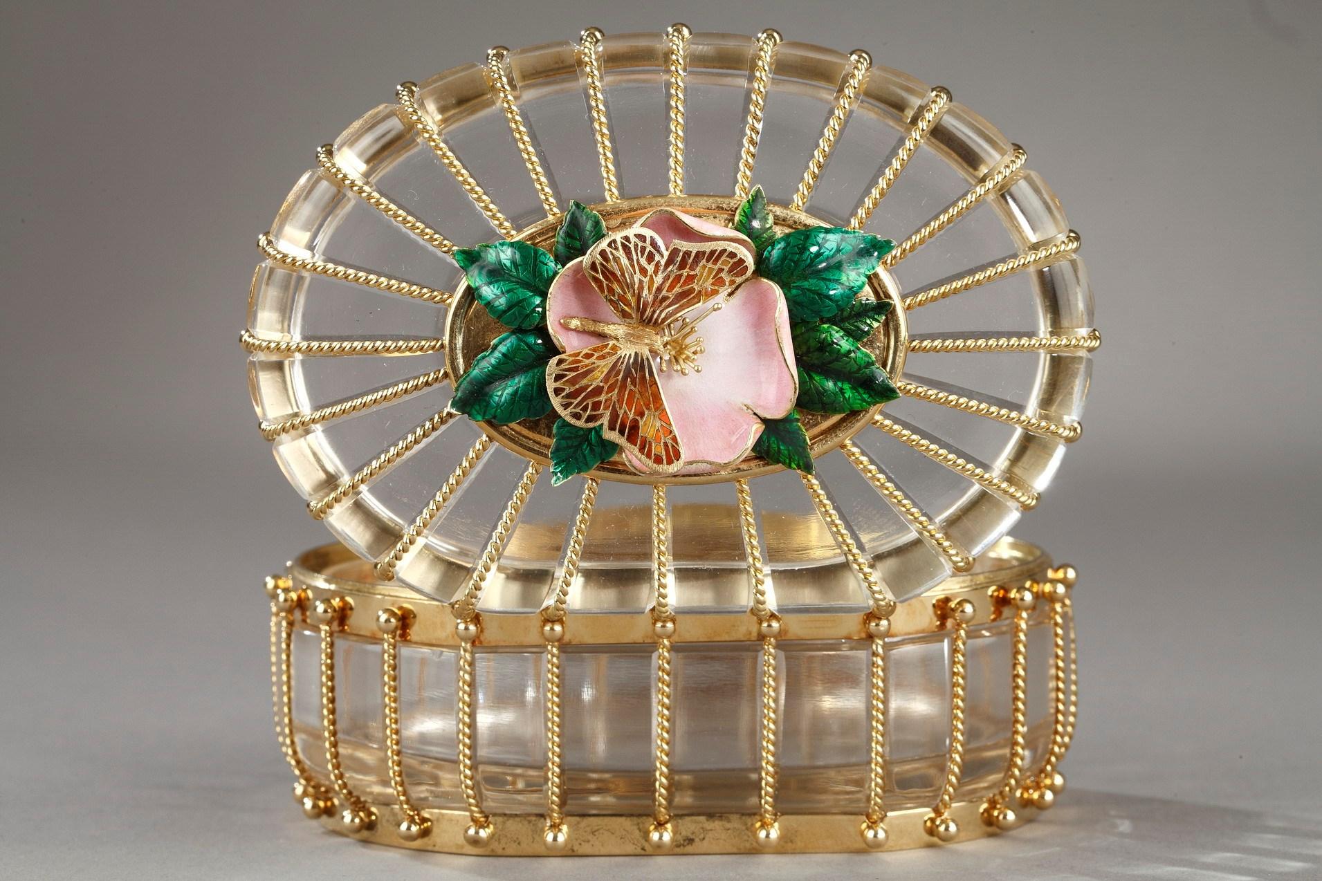 An oval, the lid applied with a pink enamel flower and green leaves on which rests a gold butterfly with pierced wings, twisted rope cagework mounts, the base rim engraved 'Designed & enameled by Philip Barnes, made by Ron Edwards for Algernon