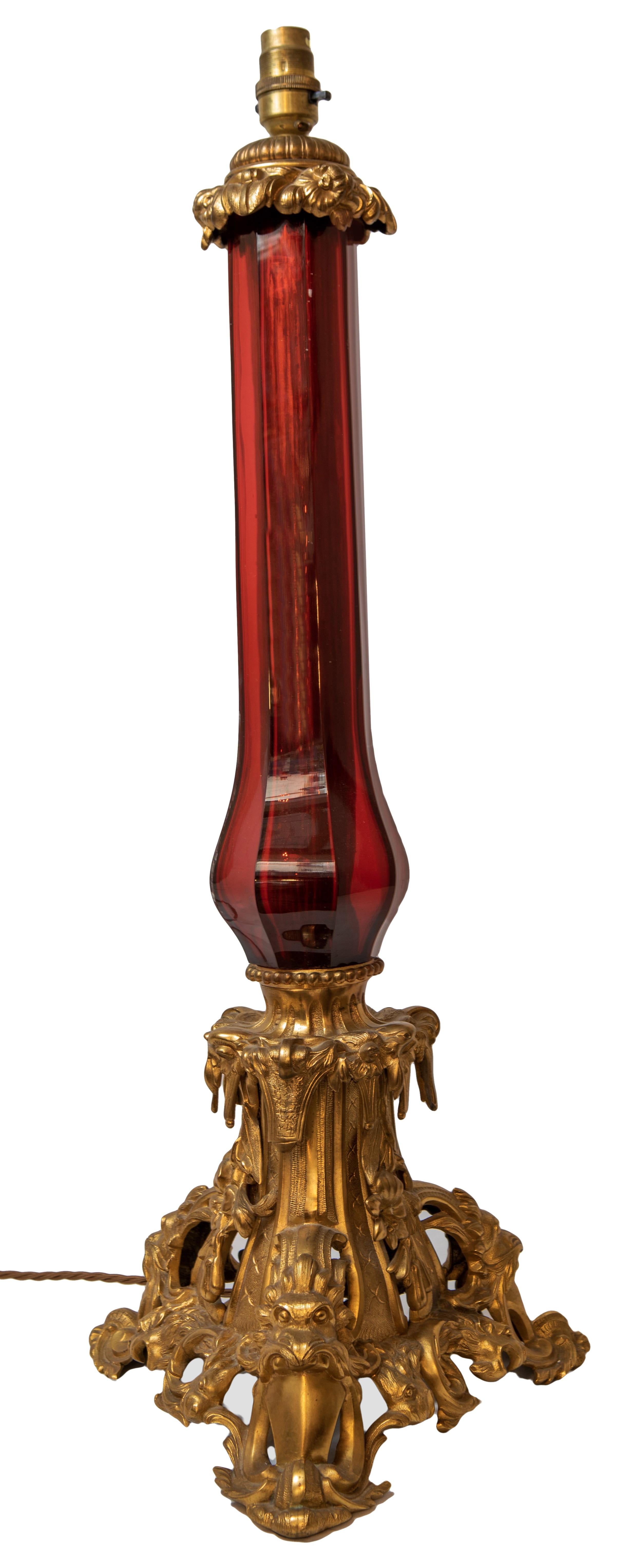 With a gilded bronze base decorated with foliage surrounding and supporting a smart cranberry glass column, including a fluted fabric shade. Fitted for electricity.
