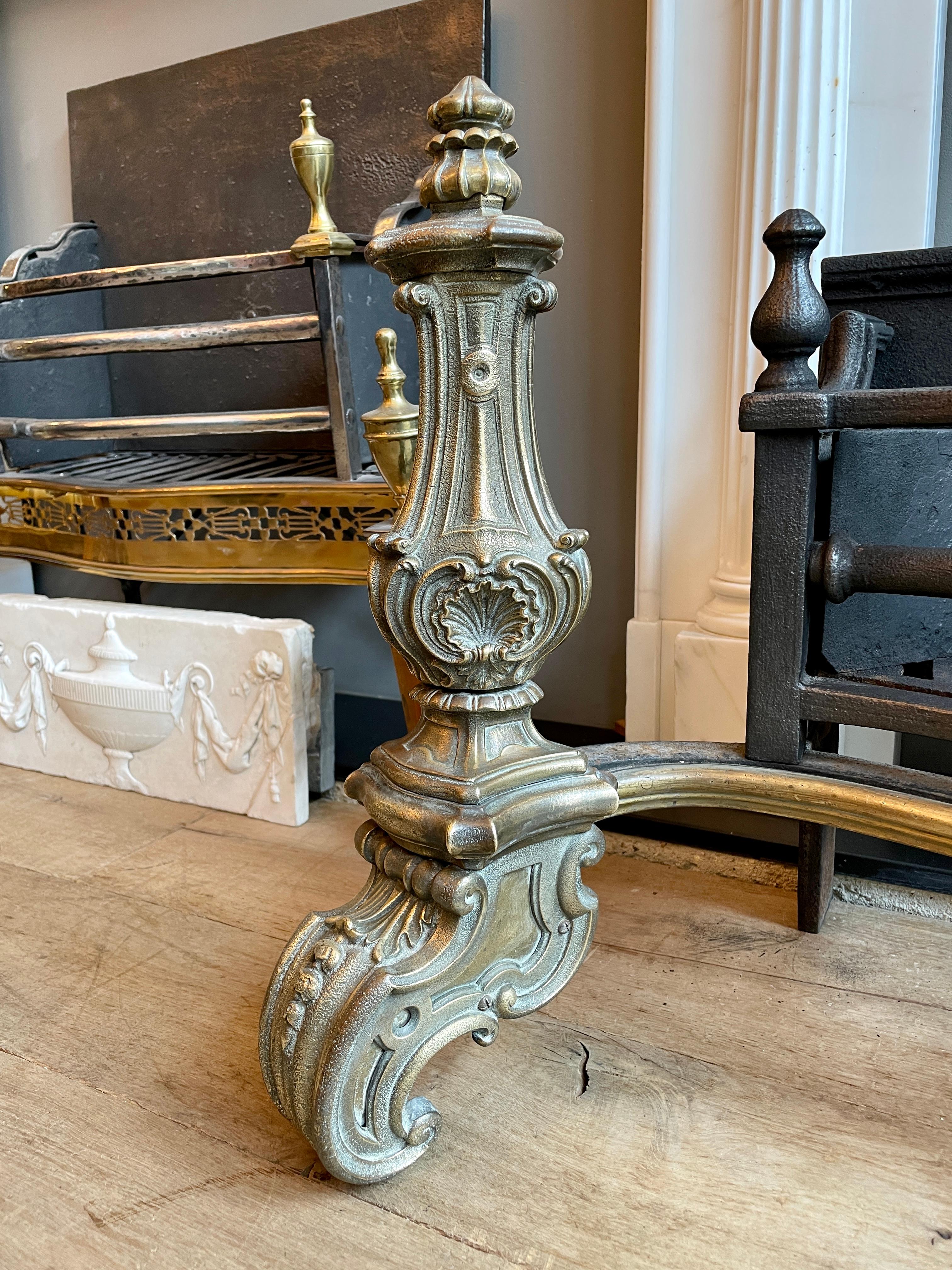 A large, opulent and substantial Rococo revival fire grate. A large burning area, with bowed bars, the top bars with finials, with a simple brass apron flanked by two impressive baluster standards with ornate decoration scrolled feet and topped with