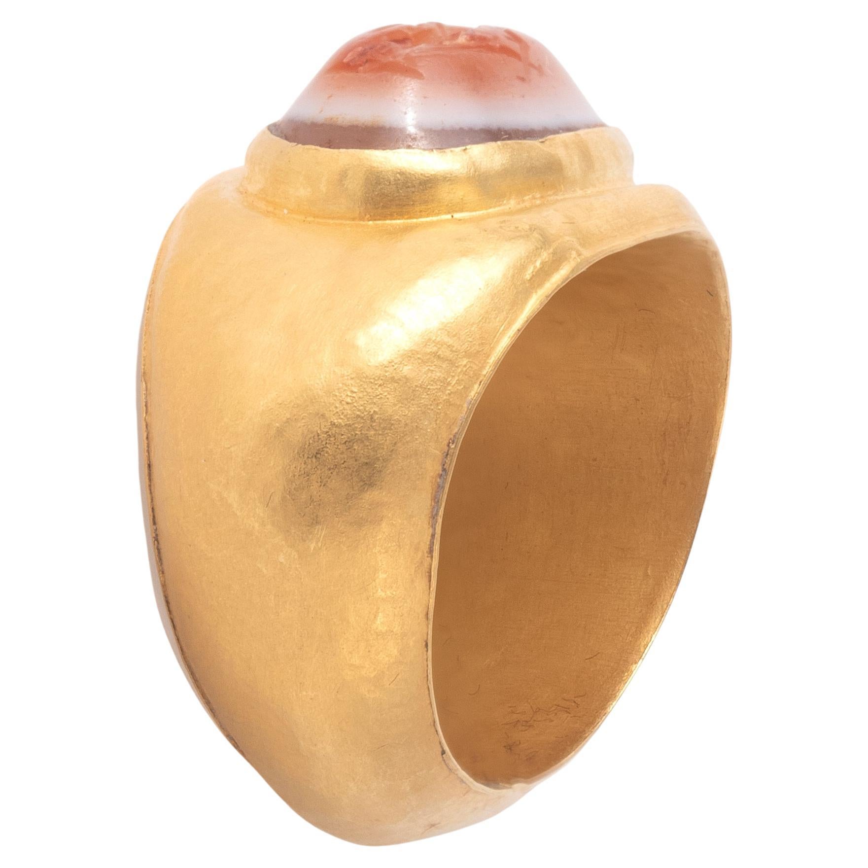 Gold ring with oval plain hoop broadening to bezel with inset with an oval banded agate intaglio with the goddess Fortuna standing in profile to the right, holding two sheaves of wheat and a ship's rudder in one hand, a cornucopia in the other, on a