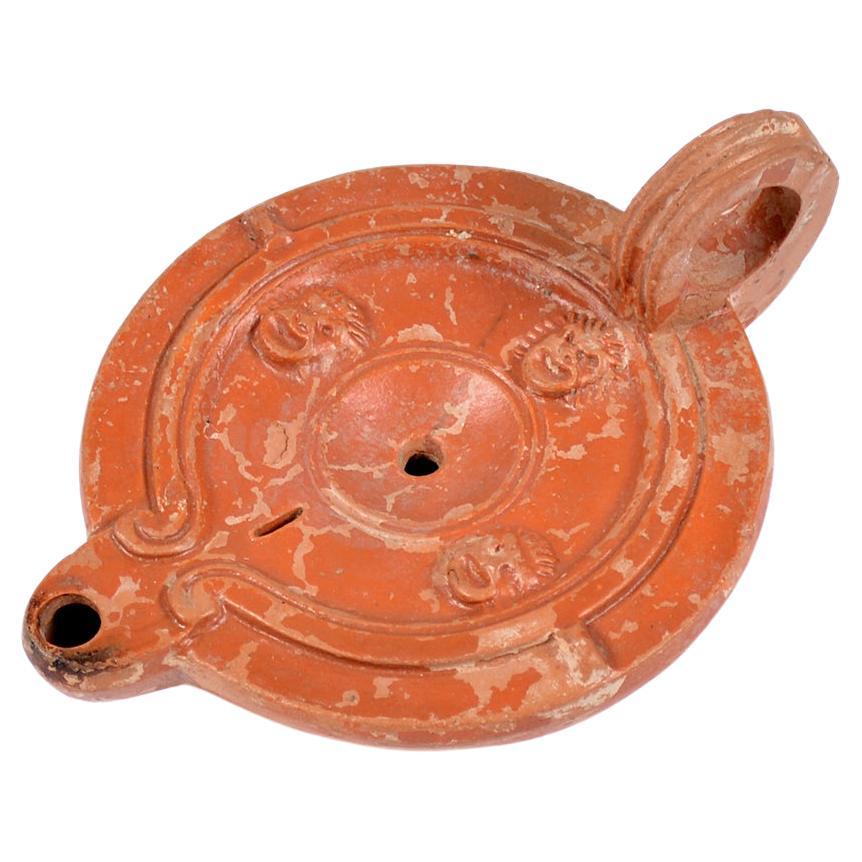 A Roman terracotta red slip ware oil lamp with theatre masks For Sale