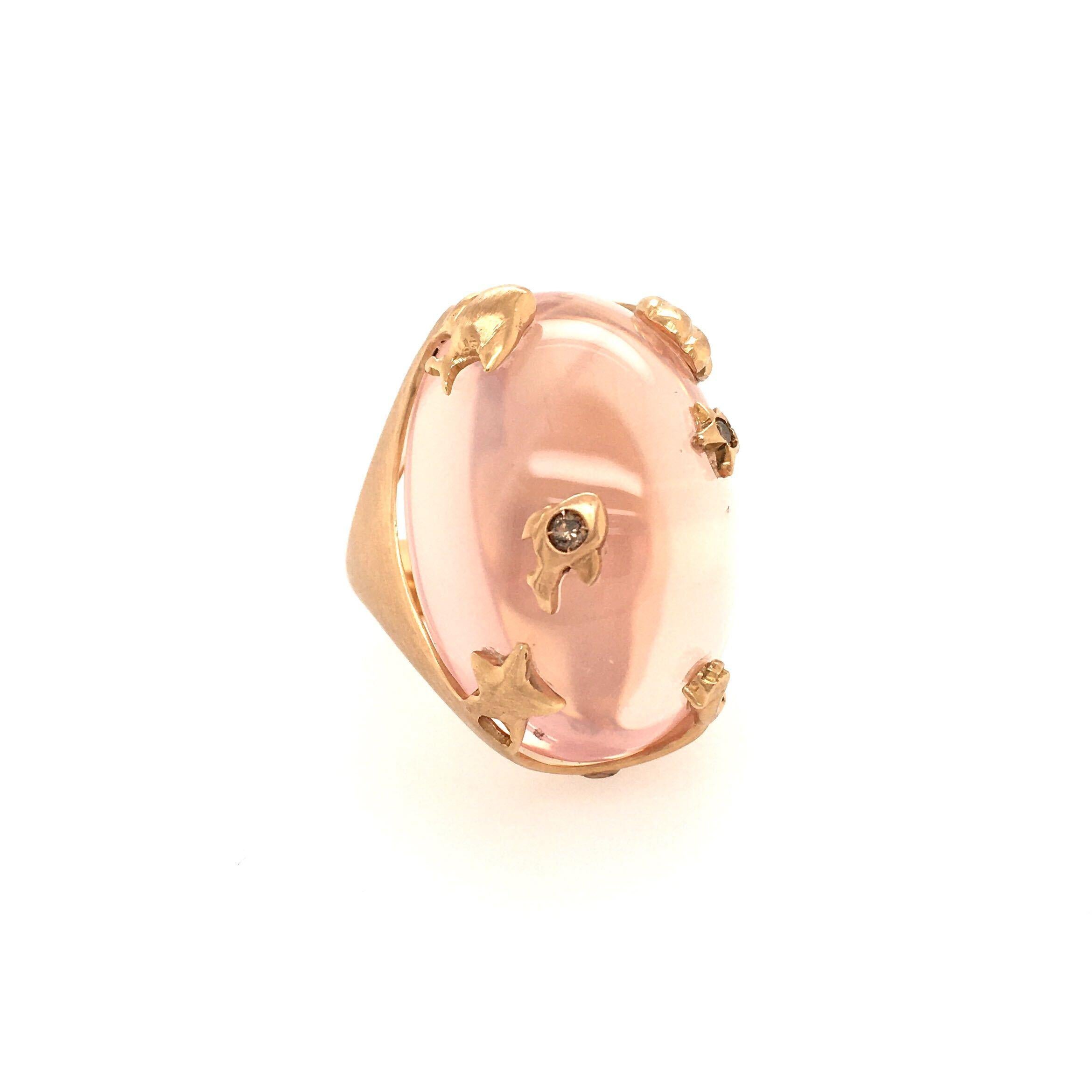 An 18 karat rose gold, rose quartz and brown diamond ring. Set with an oval cabochon rose quartz, within a brushed gold bombe mount, set with star and marine motifs, enhanced by small brown diamonds.  Size 7 1/2, gross weight is approximately 35.7