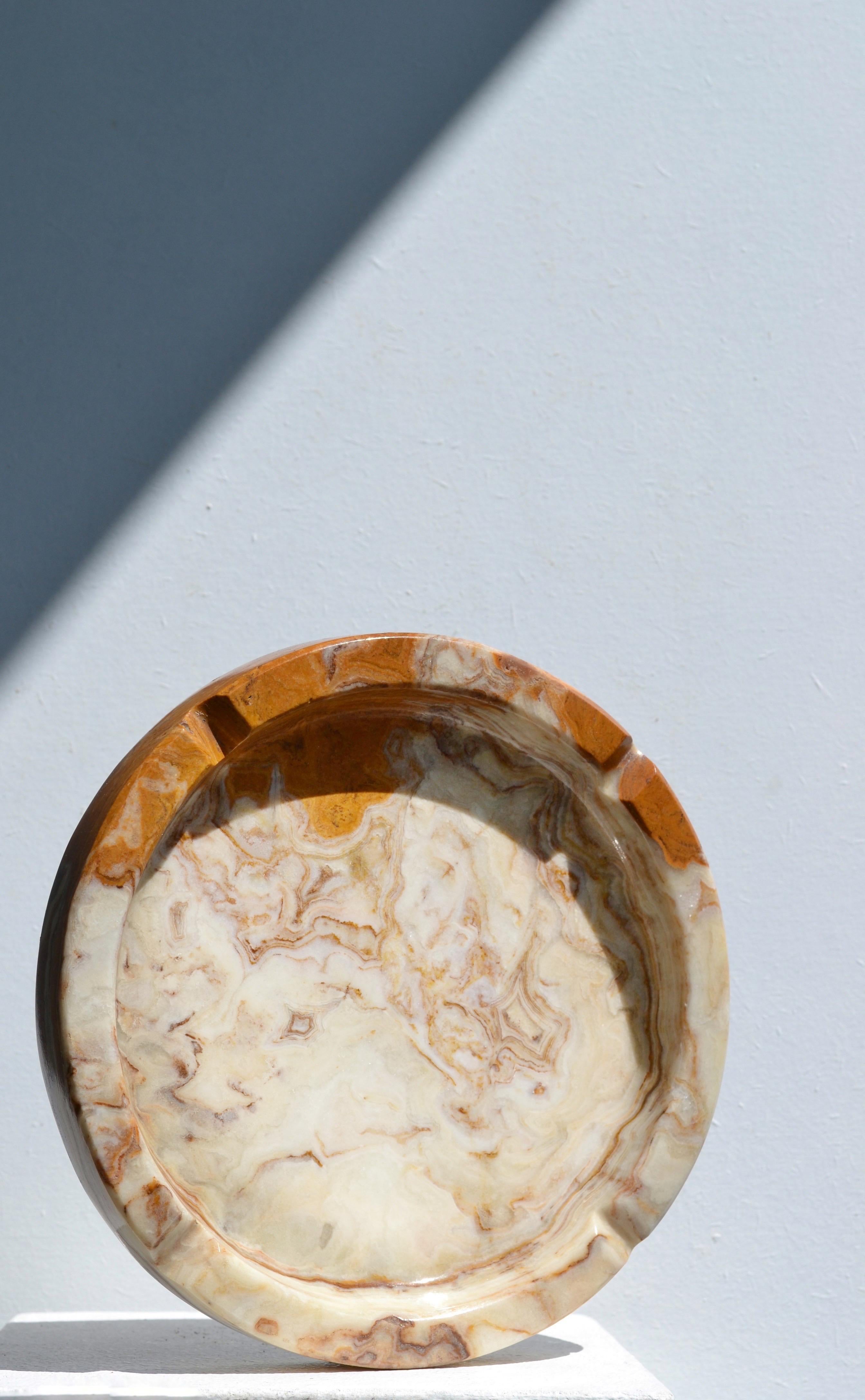 An elegant and timeless, this round ashtray is hand-carved from solid onyx, showcasing the natural beauty of the stone with warm tones of beige, cream, and soft brown. The smooth, polished surface and gentle veining highlight the mineral’s organic