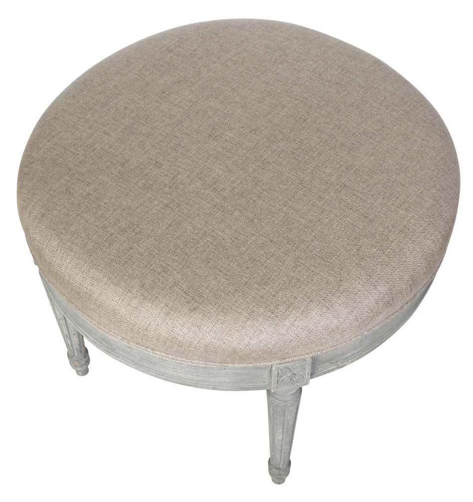 This small round ottoman has a grayish white painted base.  Its carved apron and round, tapered legs are characteristic of the Louis XV style.  The top is upholstered in a neutral linen, making it ready to go into any color scheme.