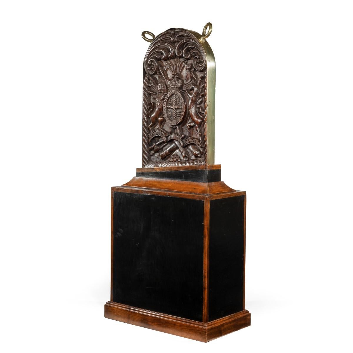 A Royal Naval ship’s elm companionway board, of rectangular form with an arched top and two sturdy brass rings, naively carved with a crowned coat of arms flanked by a lion and unicorn against a panoply of arms, all below bold confronting C-scrolls,