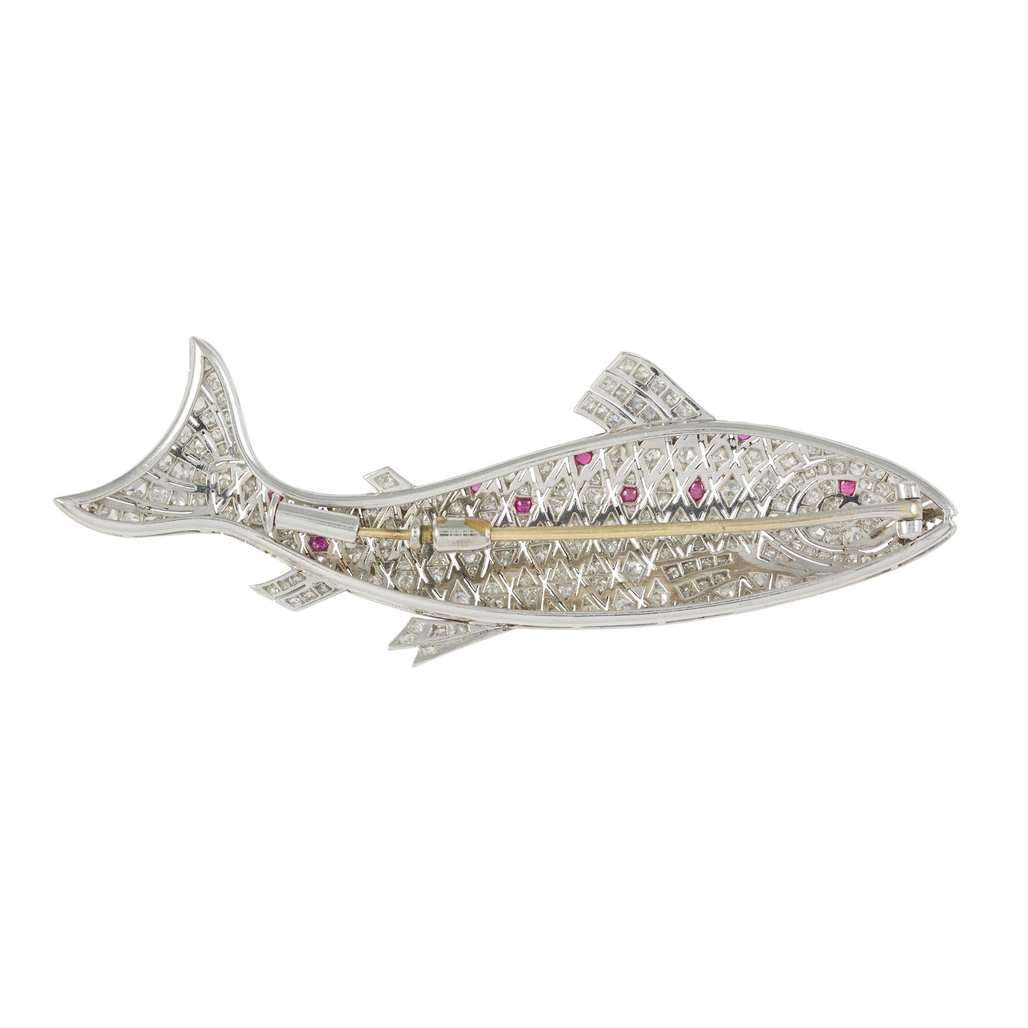 A ruby and diamond fish brooch, set with old brilliant-cut diamonds within pierced openwork and millegrain border forming the head, scales, tail and fins with cabochon rubies set along the back and eye, forming a body in motion, all to a platinum