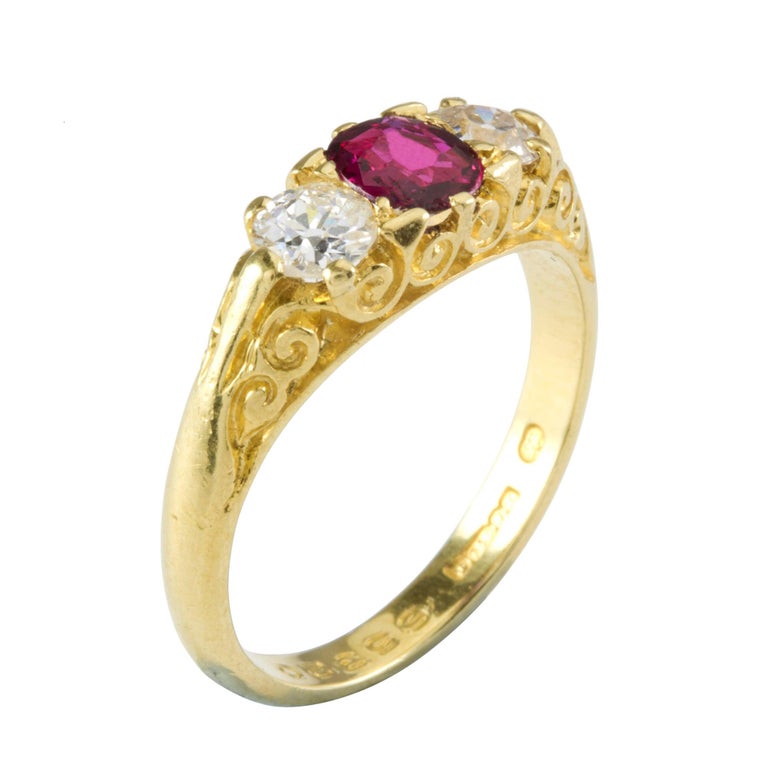 A ruby and diamond three stone ring, the cushion shape faceted ruby estimated to weigh 0.5 carats, flanked by two round brilliant-cut diamonds estimated to weigh 0.45 carats in total, all claw set to a gold mount with scroll engraved sides and