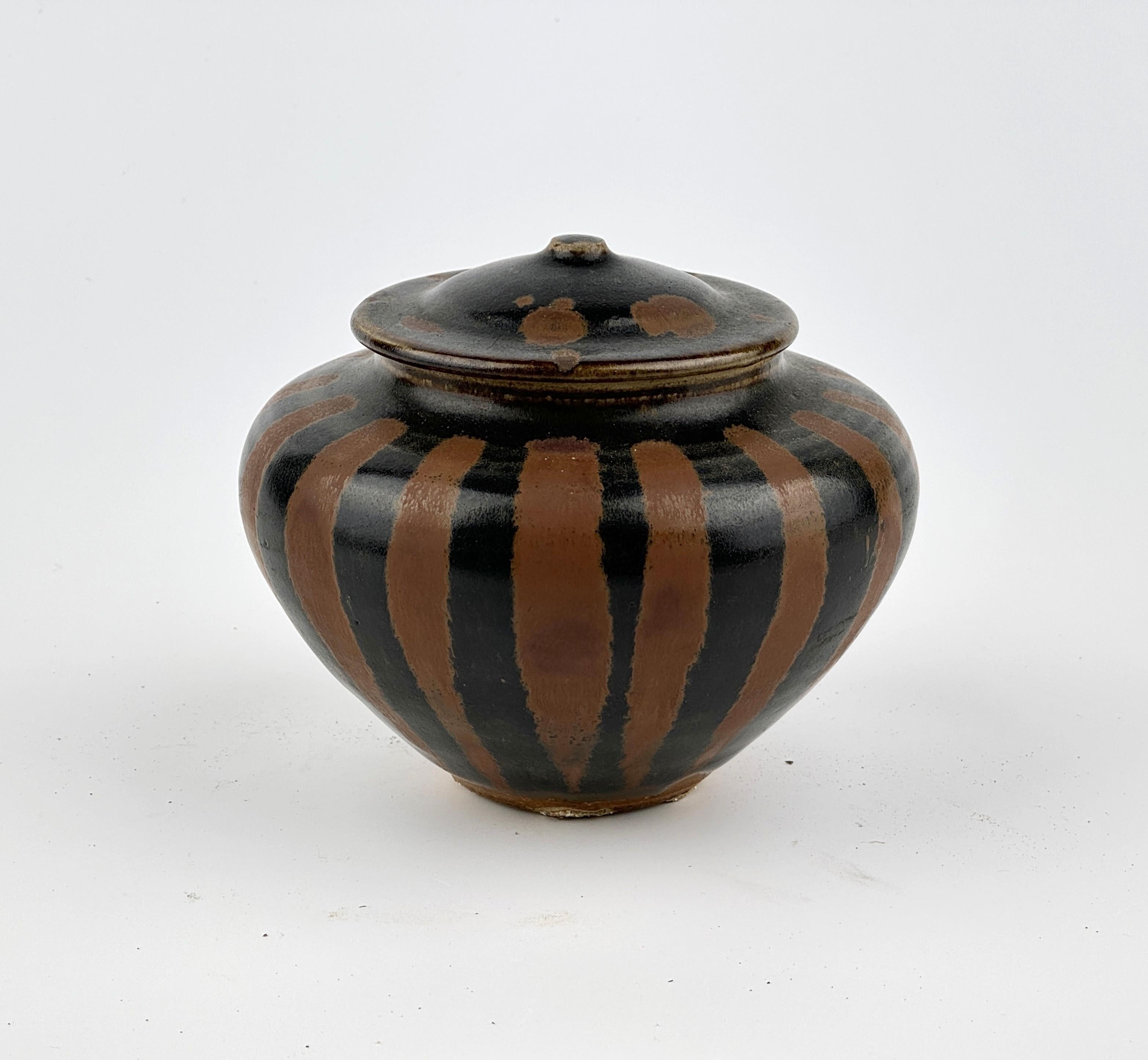Lustrous blackish-brown glaze decorated on the exterior with lines of splashes of russet color. This jar features a rounded and voluminous body, with its shoulders gently curving upward to meet the lid. The lid is topped with a small knob-like