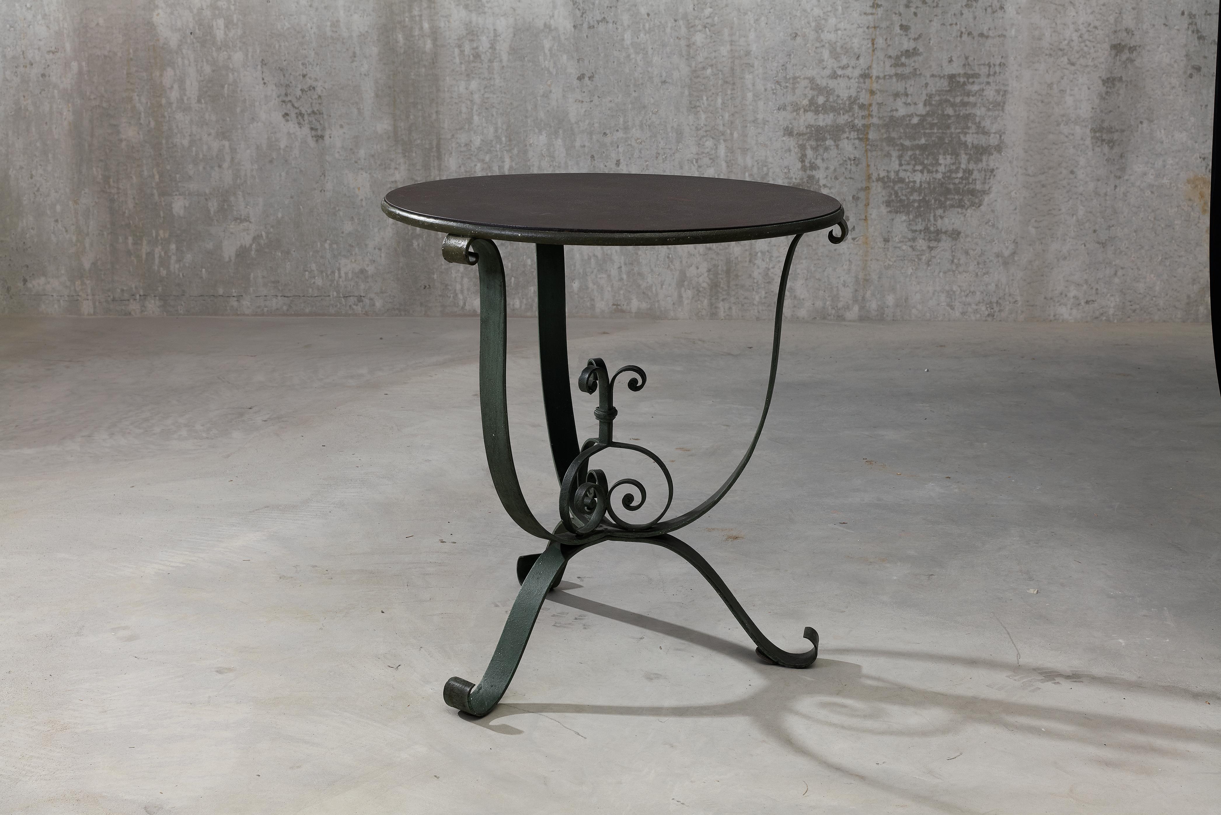 An elegant French wrought iron garden table from the 1920s or 1930s. A brown, rust colored patinated round table top is placed on three green patinated scrolling legs, with a decorative scroll decoration between the table legs. The original patina