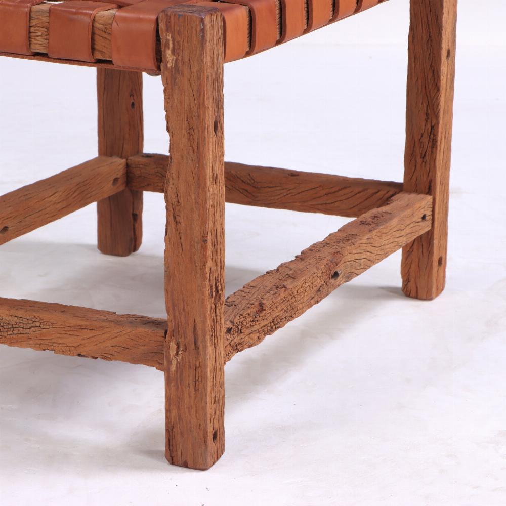 Con un armazón de madera hecho a mano con bastidor de cajón y un asiento de cuero trenzado, el banco presenta una pátina desgastada por el tiempo que habla de su antigüedad y autenticidad, y el cuero natural ofrece textura y comodidad. Robusta pero