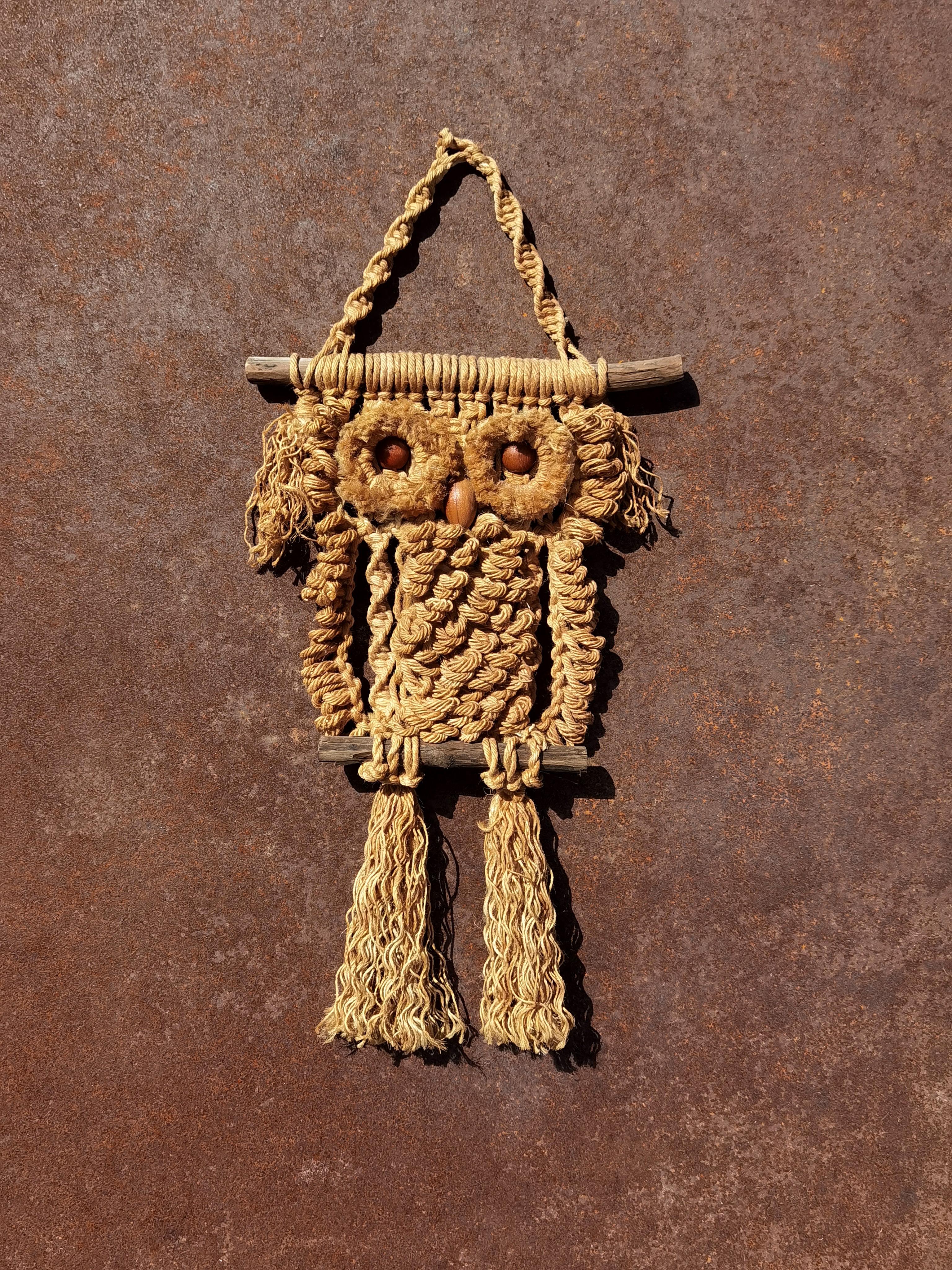 One (of a pair) sculpture or wall hanging representing a stylized owl, Handcrafted, Brutalist, Tribal, Modern Rustic, Hippie, Seventies, composed of braided rope(s) of varying thickness and quality(s) mounted on a suspended wooden structure/branch,