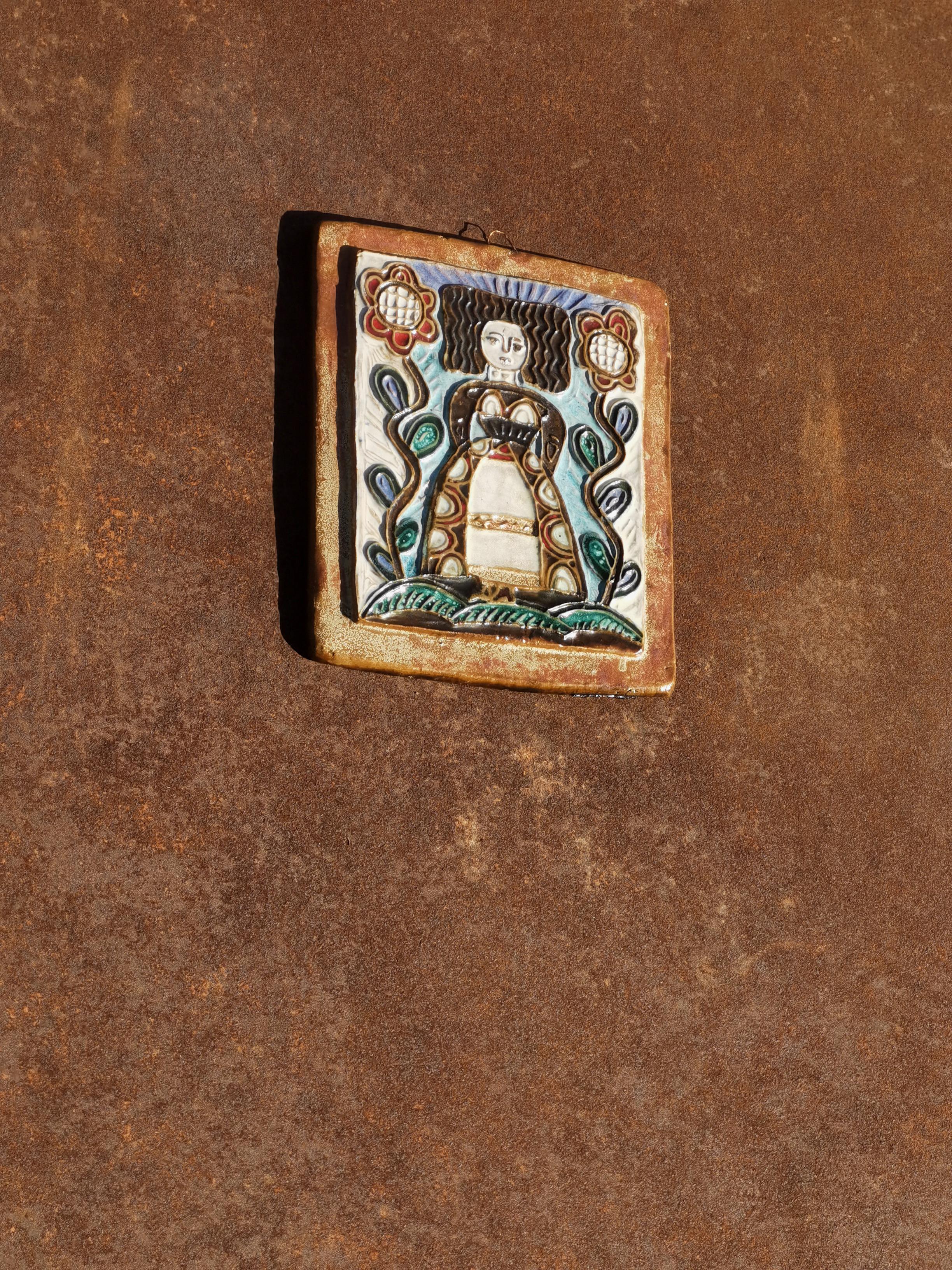 Bella obra figurativa en relieve, modernista, rústico-moderna, representación estilizada de una mujer con un tocado bretón estilizado con grandes flores, realizada en relieve sobre un rectángulo de cerámica gruesa, firma con un sello en el reverso,
