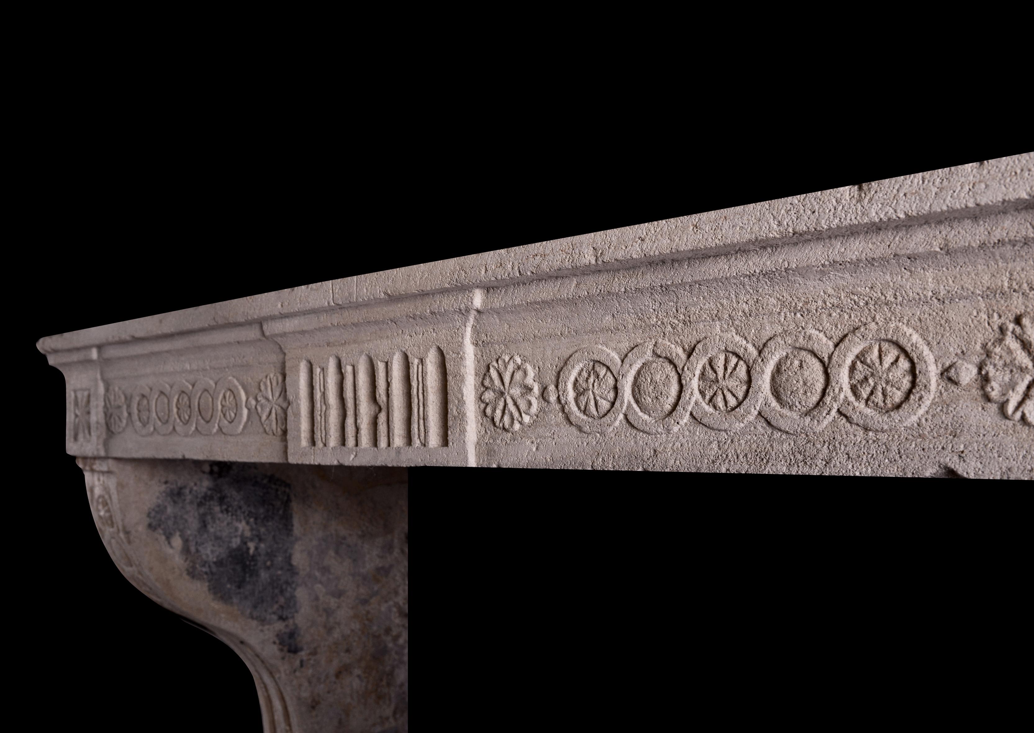 A rustic period Louis XVI stone fireplace. The shaped jambs with stop-flutes, surmounted by guilloche pattern above. The frieze with fluted centre plaque, flanked by carved rosettes and guilloche motif. Moulded shelf above. Particularly tall scale,