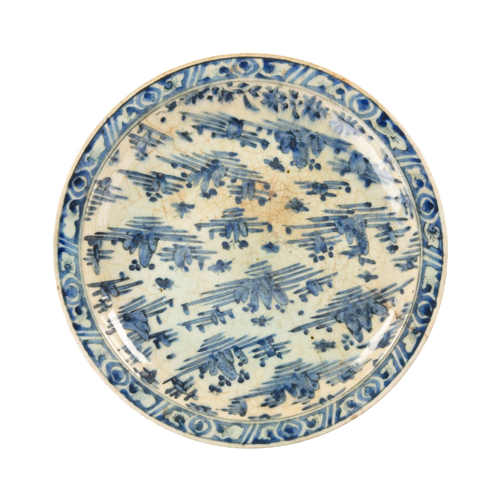 A Safavid blue and white pottery dish, of shallow circular form decorated in underglaze blue with scattered rocky outcrops, within a panelled rim, the reverse with stylised lappets.  Persian, 18th century.
