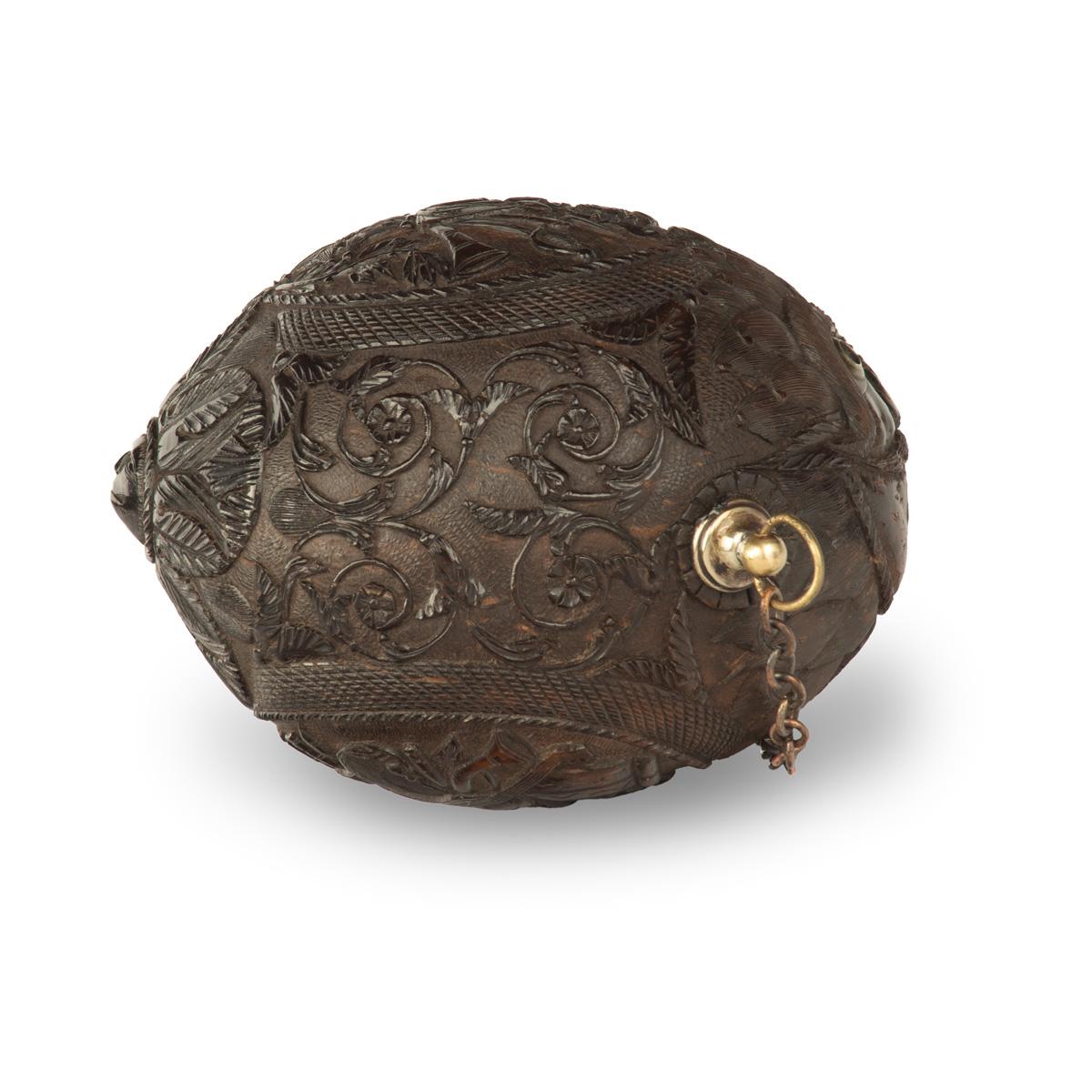 A sailor’s carved coconut Bugbear powder flask.  This carved coconut is carved with two ovals, one showing a military panoply with standards, bayonets, swords and bugles all above a five-pointed Maltese cross, the other with a musical trophy.  The