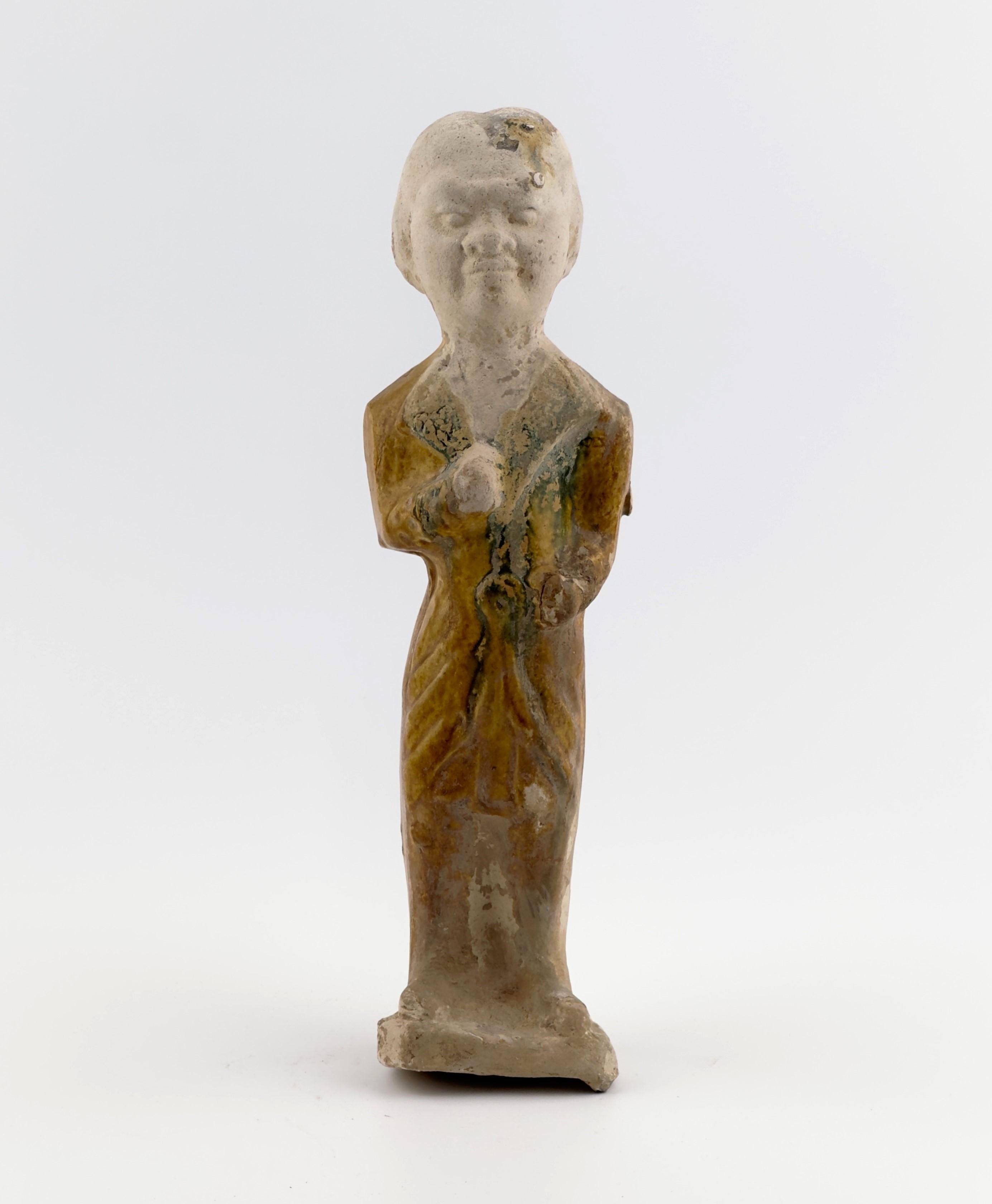 A standing figure in elongated form wearing traditional garments. The figure's stern and resolute expression symbolizes its role as a guardian of the soul in the afterlife. The figure is holding an object in its hand, though its specific details are