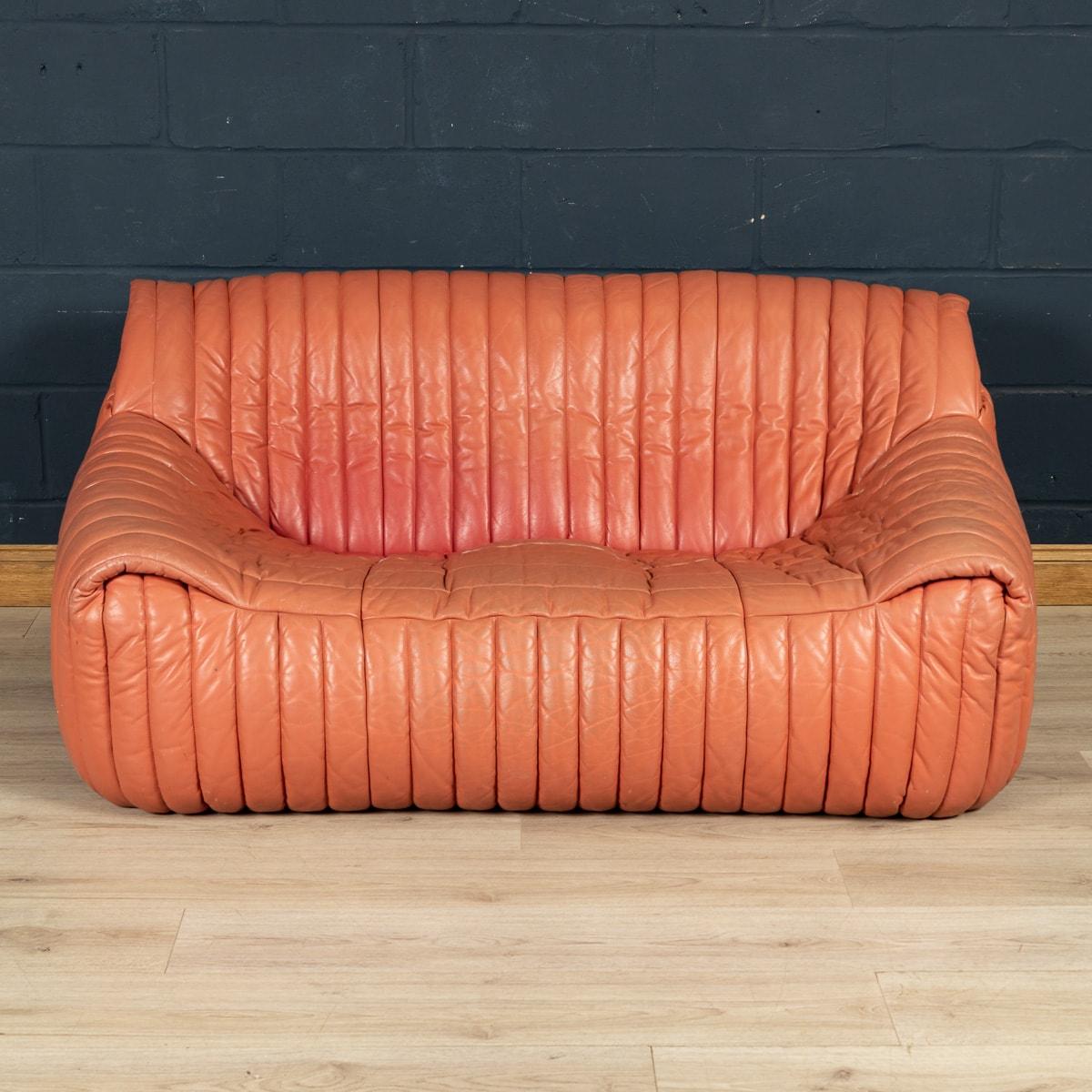 An iconic 1970s design, the Sandra sofa was designed by Annie Hiéronimus for Cinna after she joined the Roset Bureau d'Etudes in 1976. Constructed from foam, this two-seater sofa has a solid form which is fully upholstered in soft off-red ribbed
