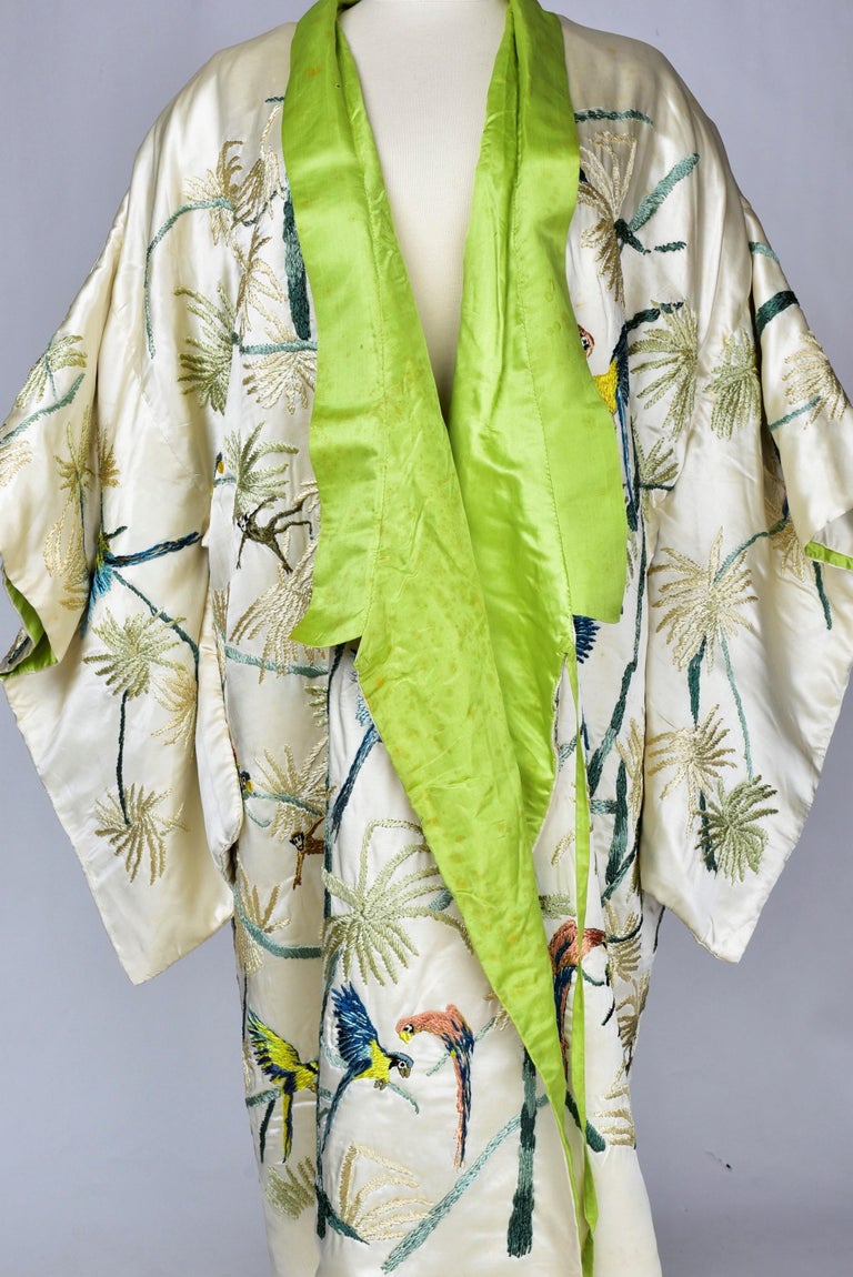 Circa 1920 -1930

France

Cream satin kimono for the evening or inside, lined with absinthe green satin and embroidered with a polychromatic decoration in exotic style. Beautiful floche silk embroidery with palm trees, parrots and chimpanzees. Loose