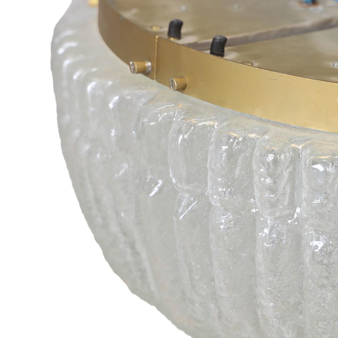 A textured glass and a brass flush mount circa 1950. The circular form is built around a central brass disk. It is surrounded by thick, ribbed glass segments with a frosted surface and visible air bubbles throughout. The glass elements are