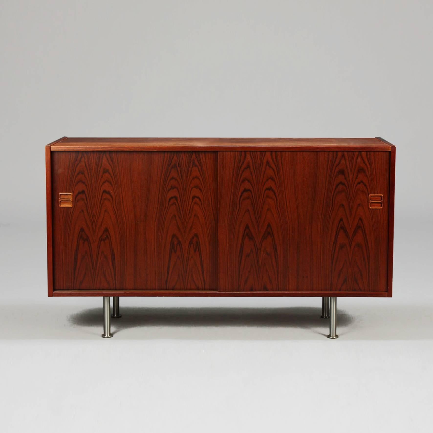 
Anpalisander sideboard of rectangular shape opening by two sliding doors on a shelf on four round steel legs.
Denmark.
Circa 1960.