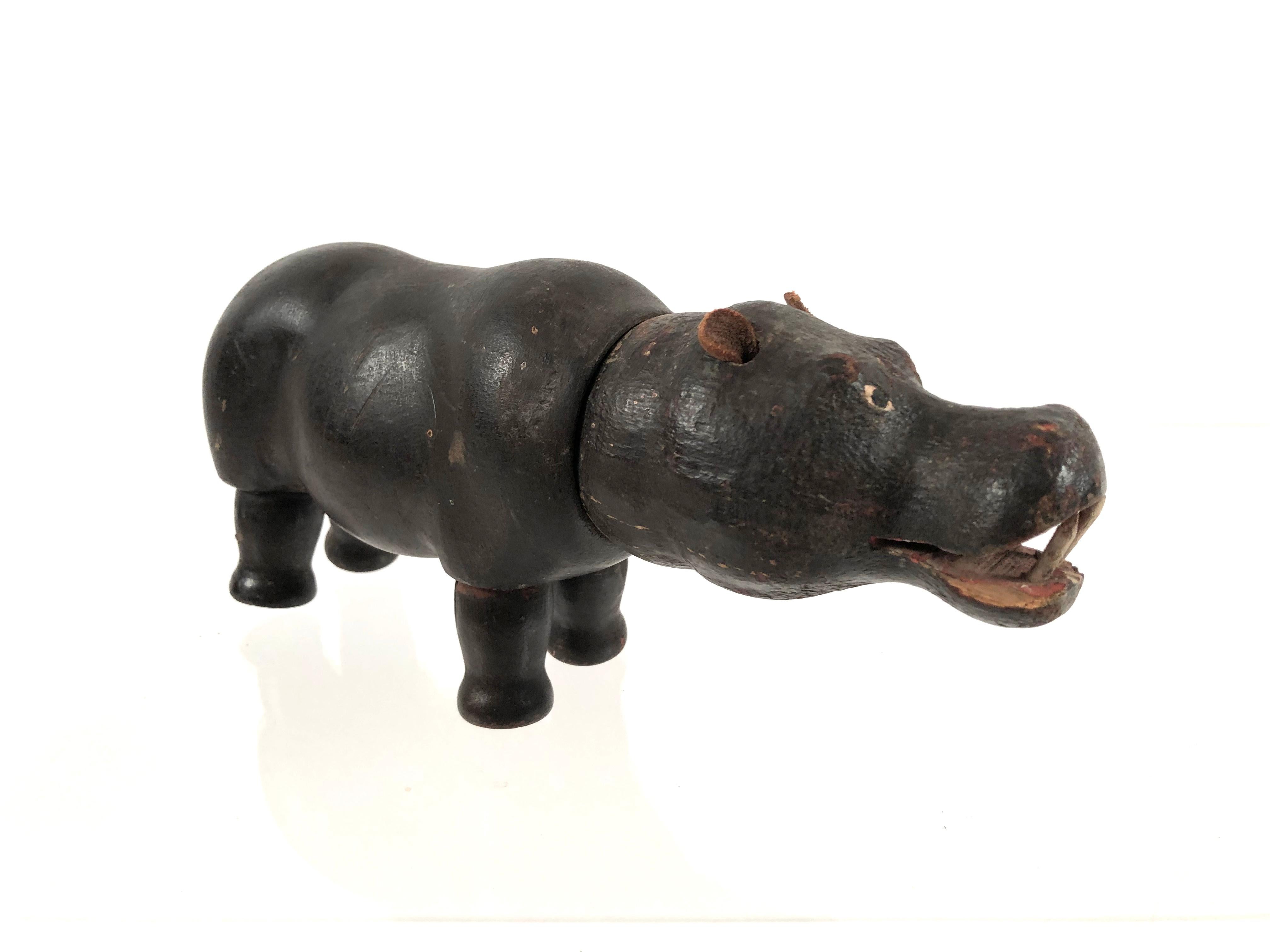 A painted wood toy hippopotamus with leather ears and articulated head and legs which rotate. Expressive face with painted eyes and large wooden tusks. Old, leathery brown painted surface. Schoenhut is a famous American toy company which was founded