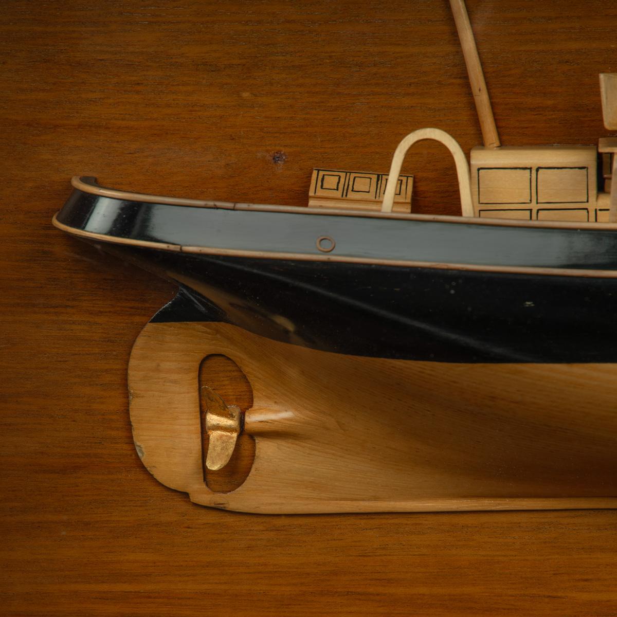 A Scottish builder’s cased half hull model of a herring drifter, the carved yellow pine hull with ebonized box sides and stringing and gilt propeller, plain decks with wooden fittings including anchor davits, cleats, cut away masts with silk swallow