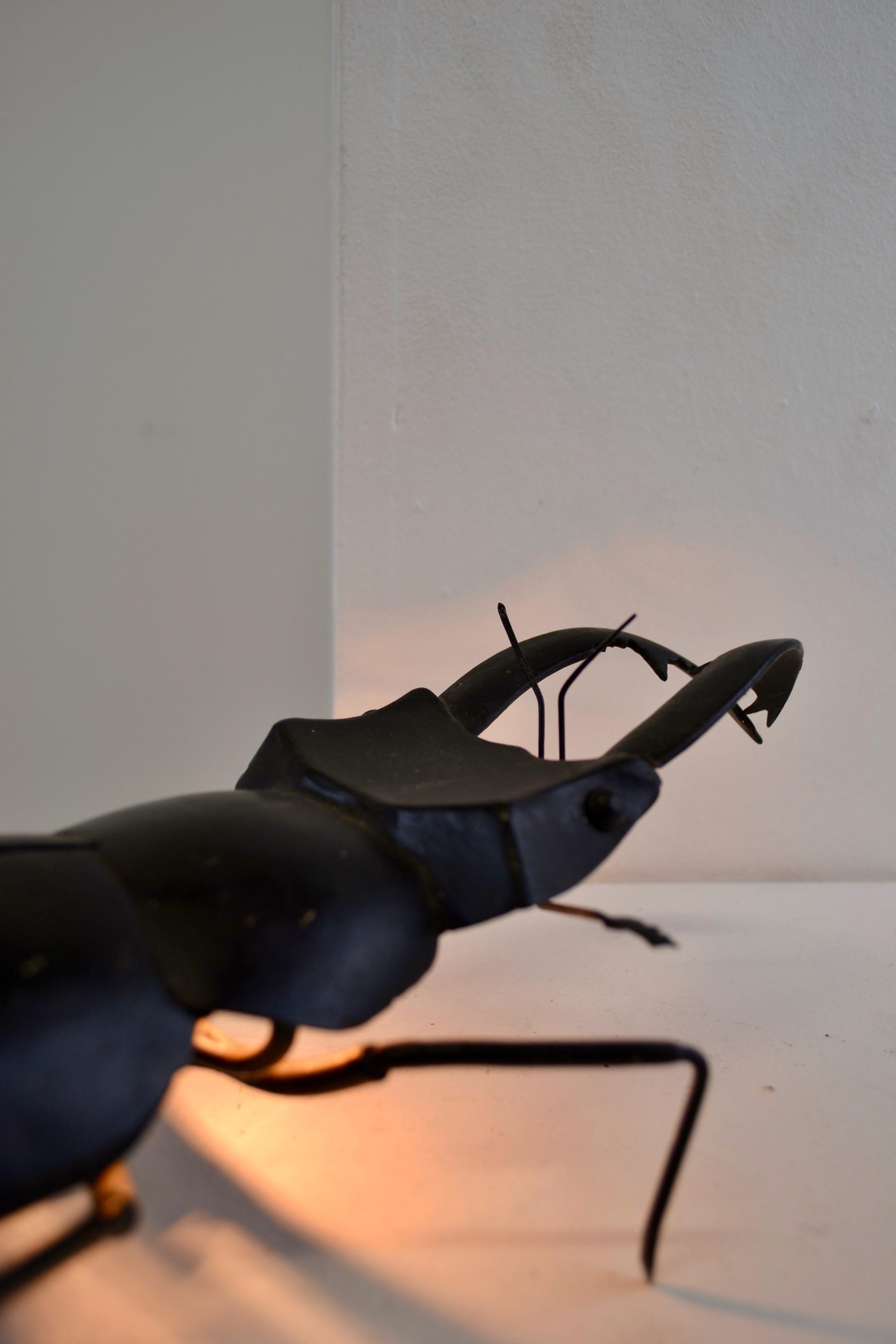 This metal lamp, dating from the 1960s, takes on a detailed insect shape, specifically a beetle with prominent pincers. Its sculptural and realistic design captures the essence of the insect with precise finishes, making each part of the body