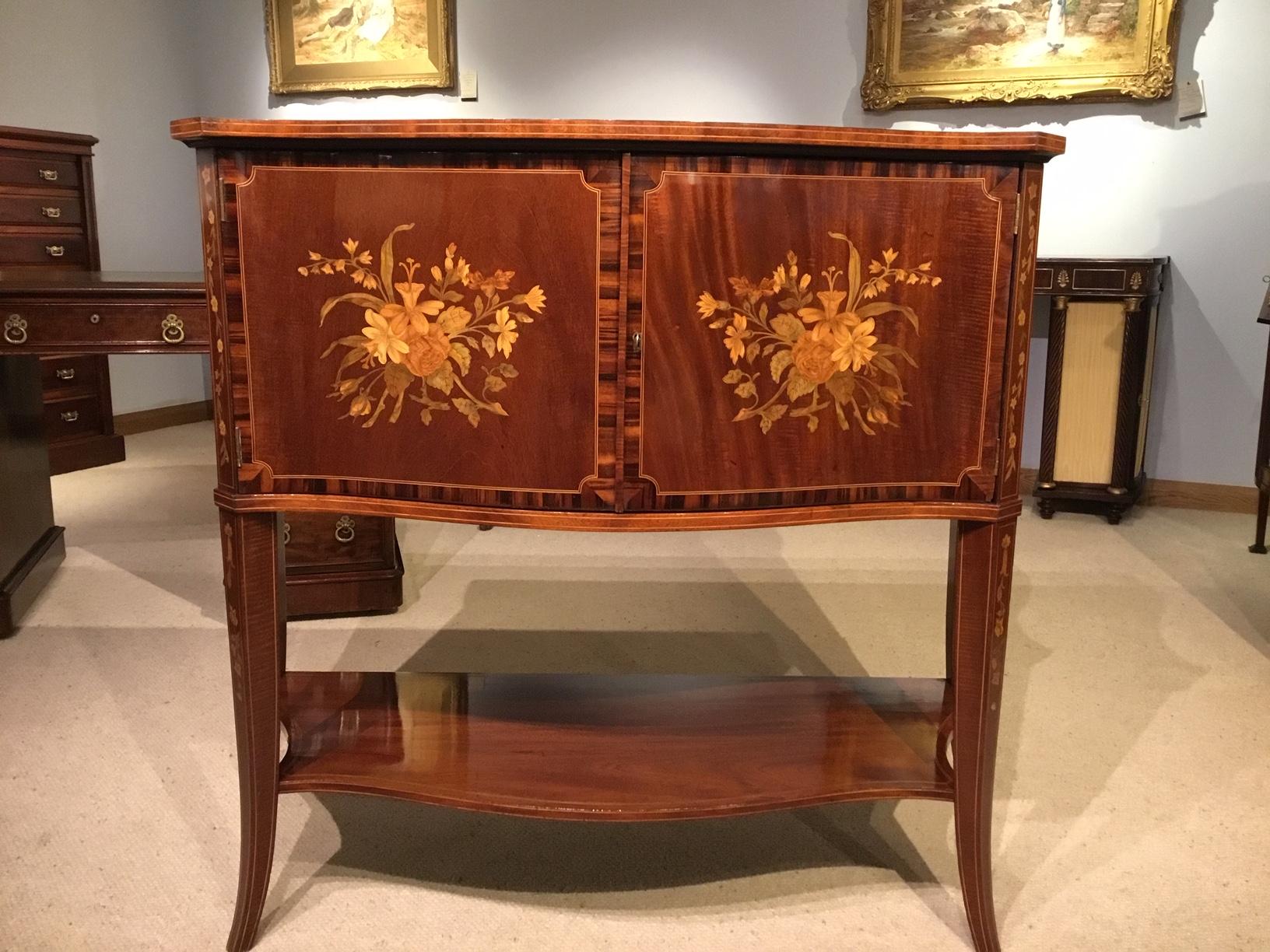 A serpentine shaped Edwardian period marquetry inlaid side cabinet. Having a fiddle back mahogany top of serpentine outline with fine marquetry and pen-work floral detail, cross banded in coromandel. The front having two serpentine shaped doors,