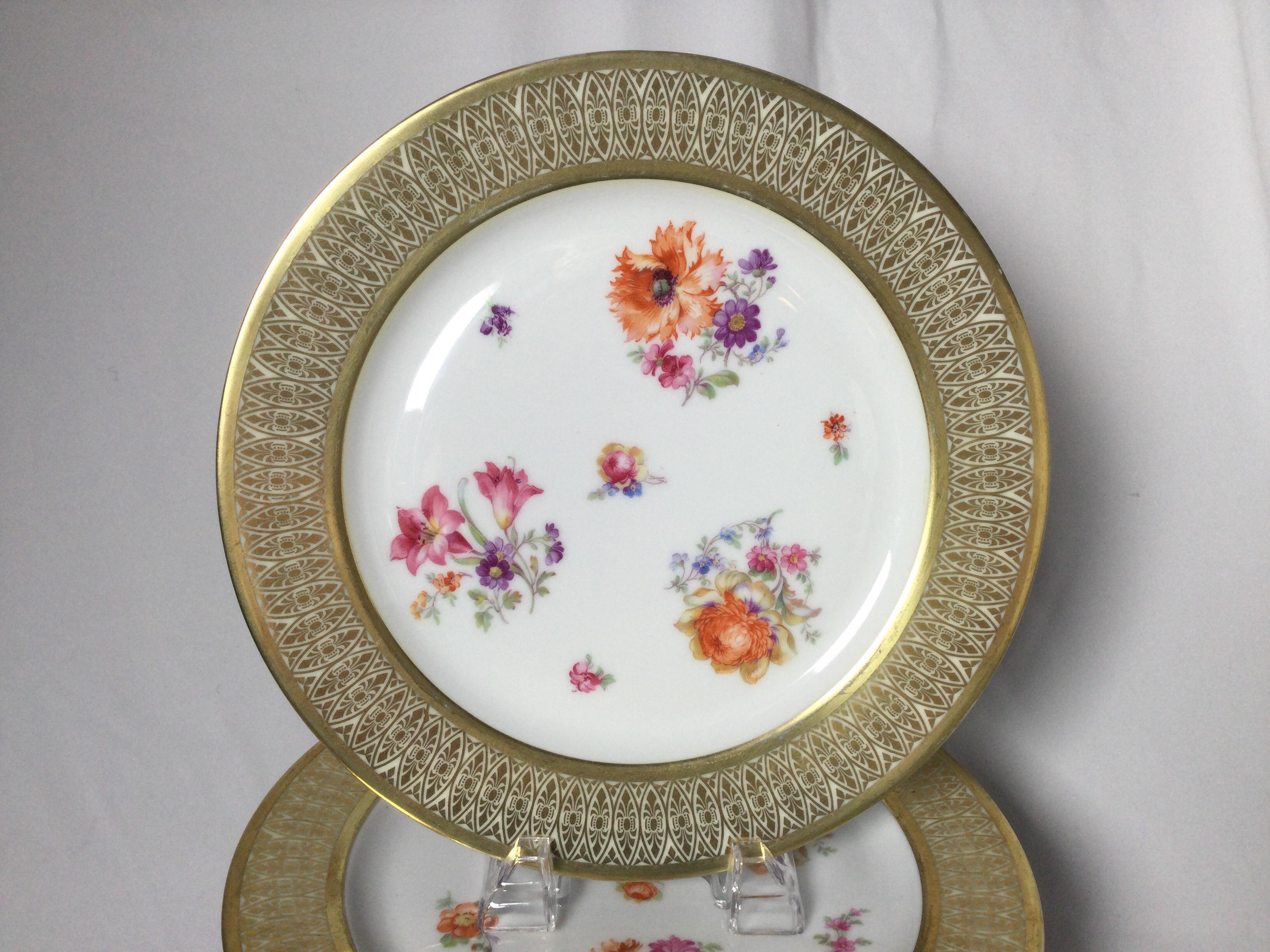 A beautiful set of 12 porcelain 10.75 inch service plates with elaborate gold borders. The floral centers with lacy style borders each with slightly different bouquets and sprigs of Dresden style flowers.