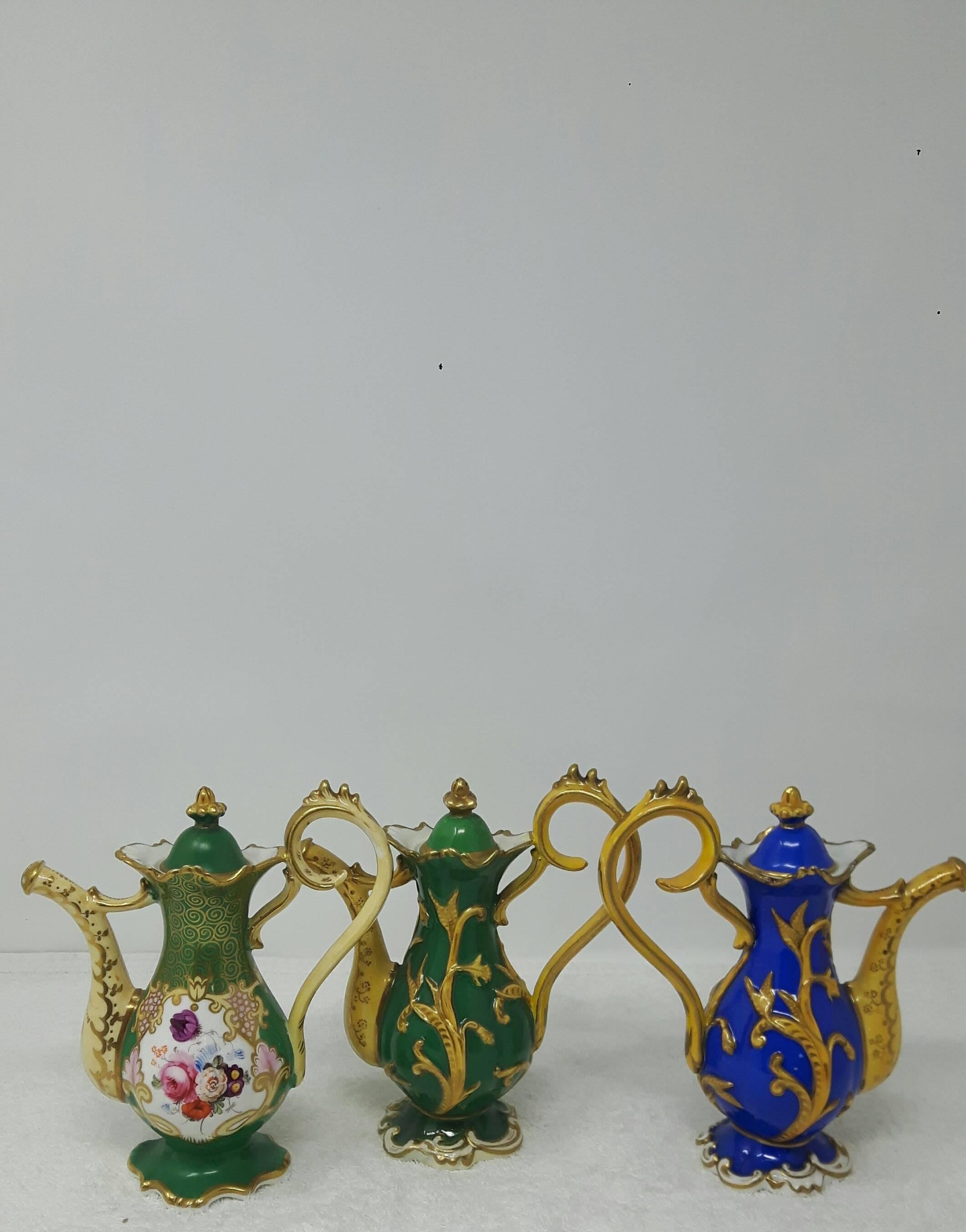 A trio of ewers from the Ridgway factory. The first pot is hand-painted with flower bouquets on a green background with an elaborate handle and spout, the finial is in the shape of a crown

The second coffee pot is identical in shape and colour